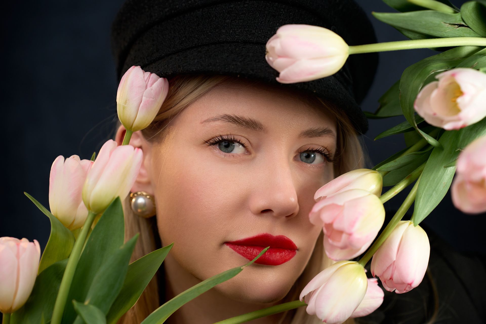 A woman in a black hat is holding a bouquet of pink tulips.