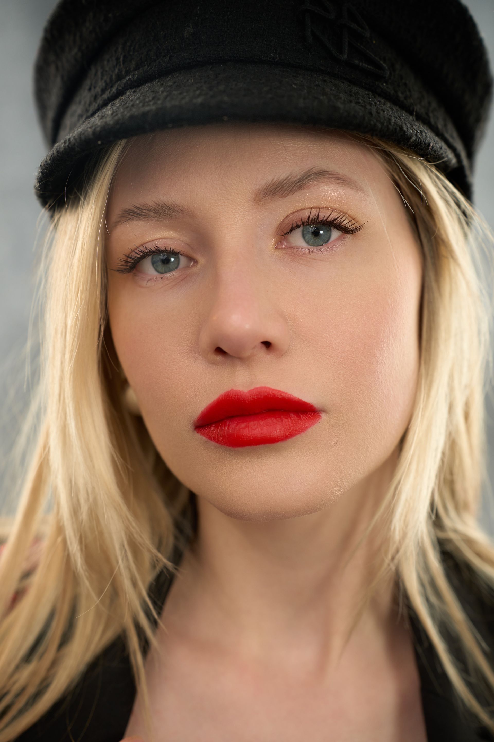 A close up of a woman wearing a black hat and red lipstick.