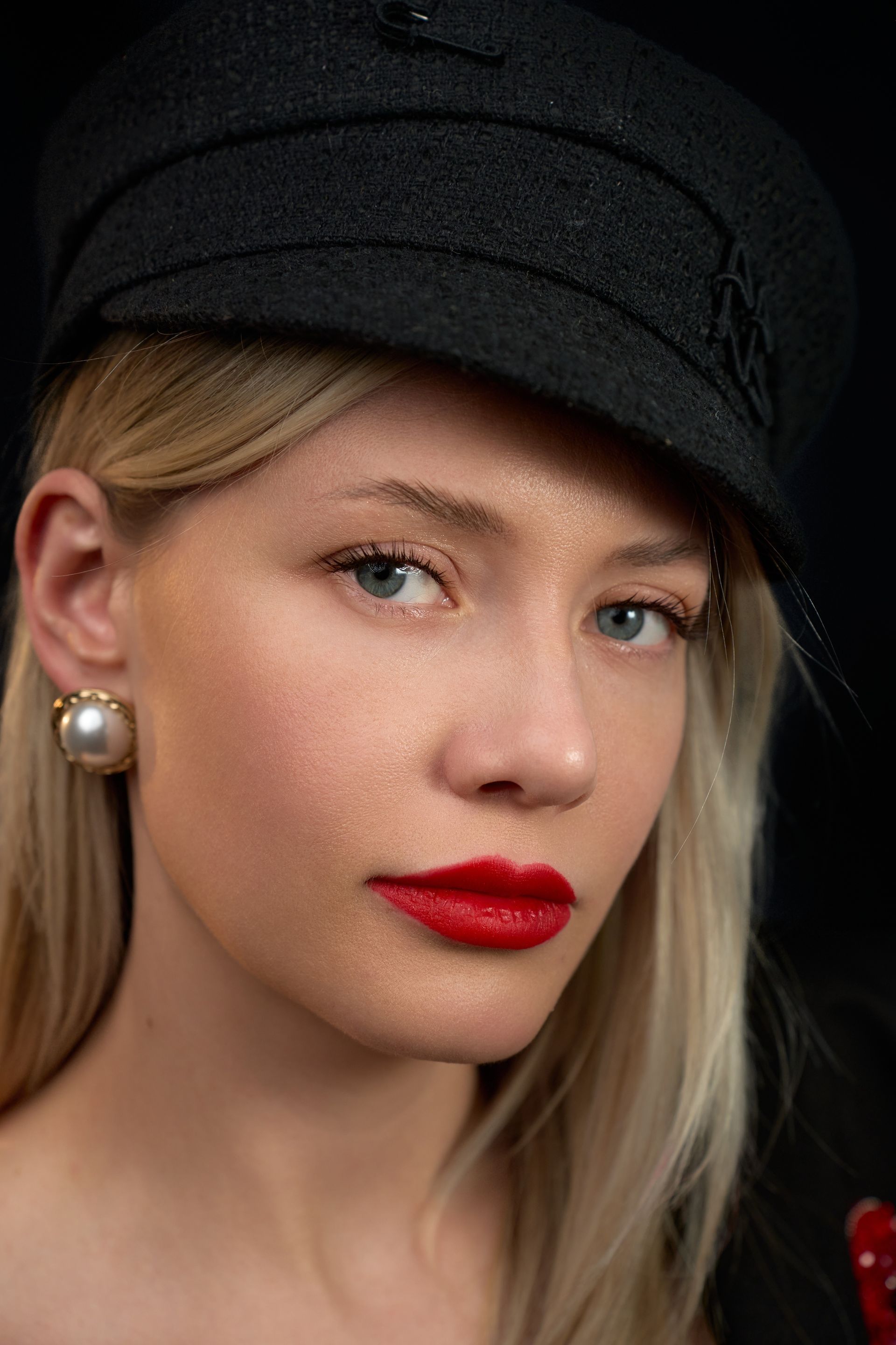 A woman wearing a black hat and red lipstick is looking at the camera.