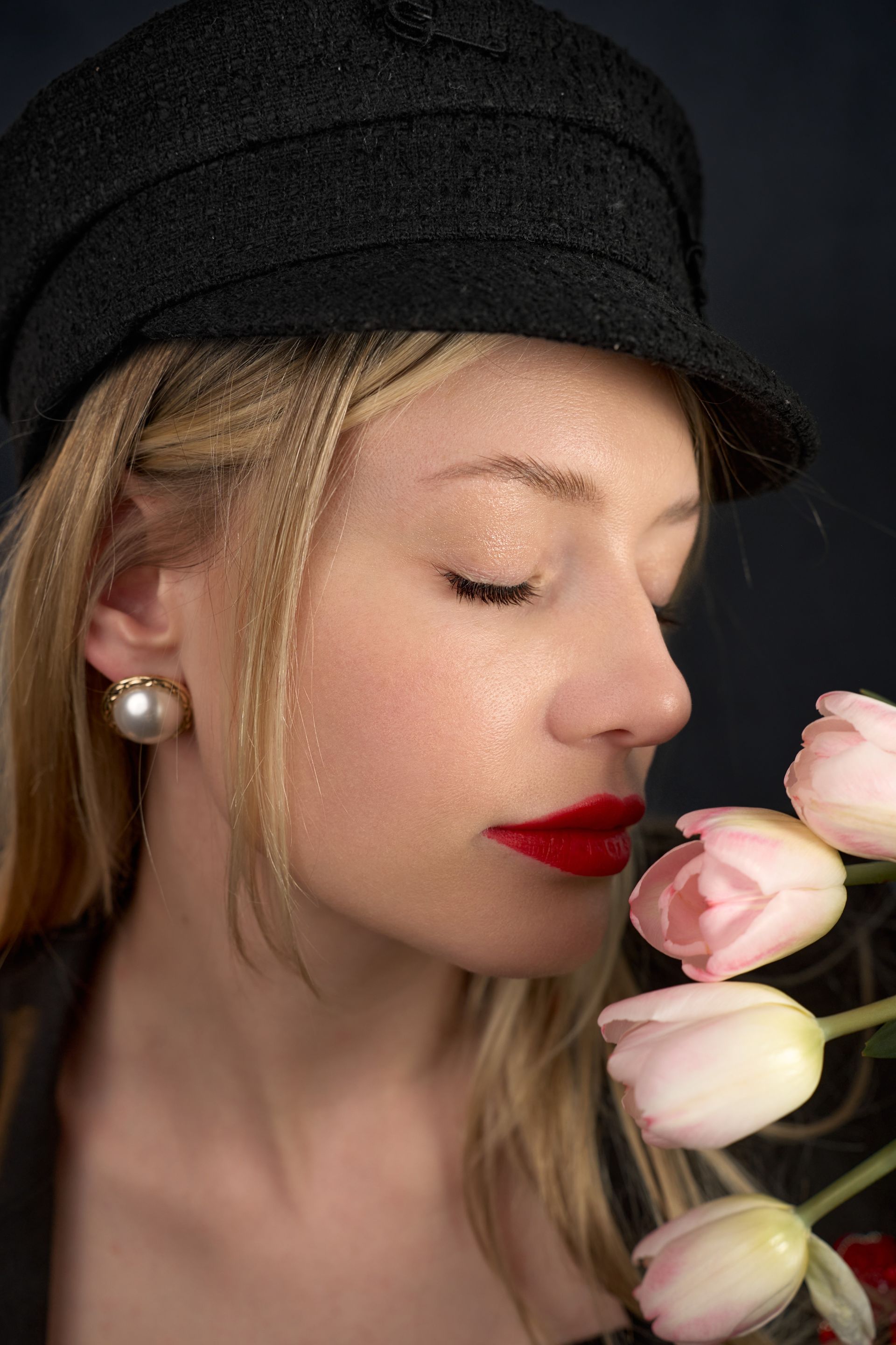 A woman wearing a hat and earrings is smelling pink tulips.
