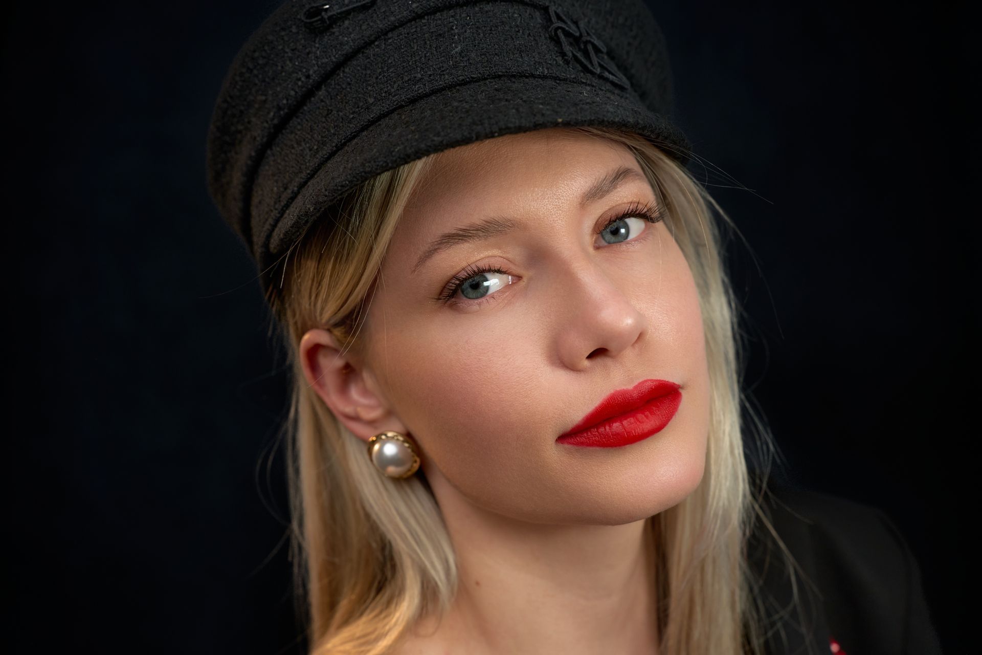 A woman wearing a hat and red lipstick is looking at the camera.
