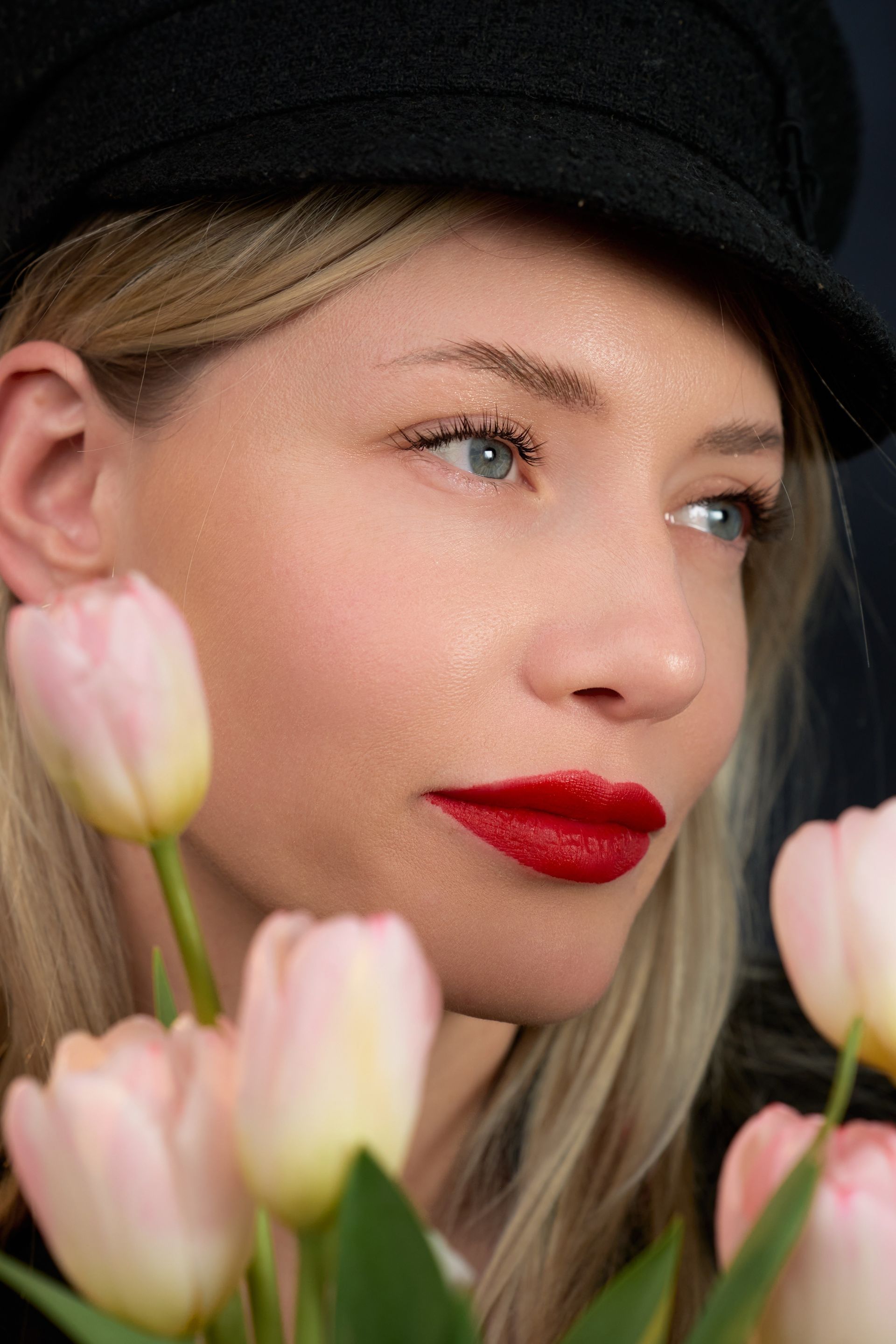 A woman wearing a hat and red lipstick is holding a bouquet of pink tulips.