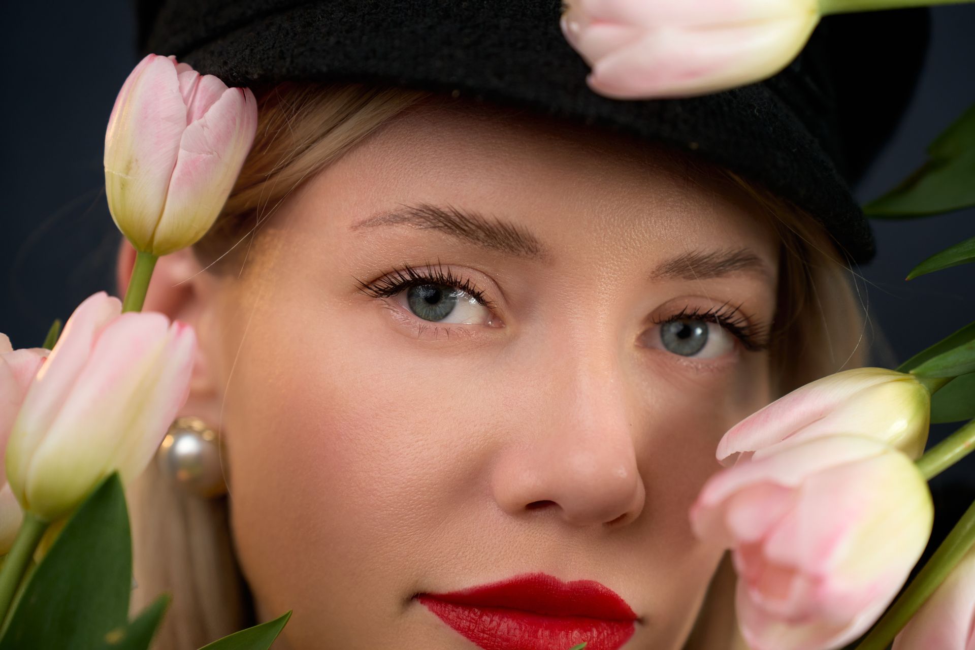 A woman wearing a hat and red lipstick is surrounded by pink tulips.