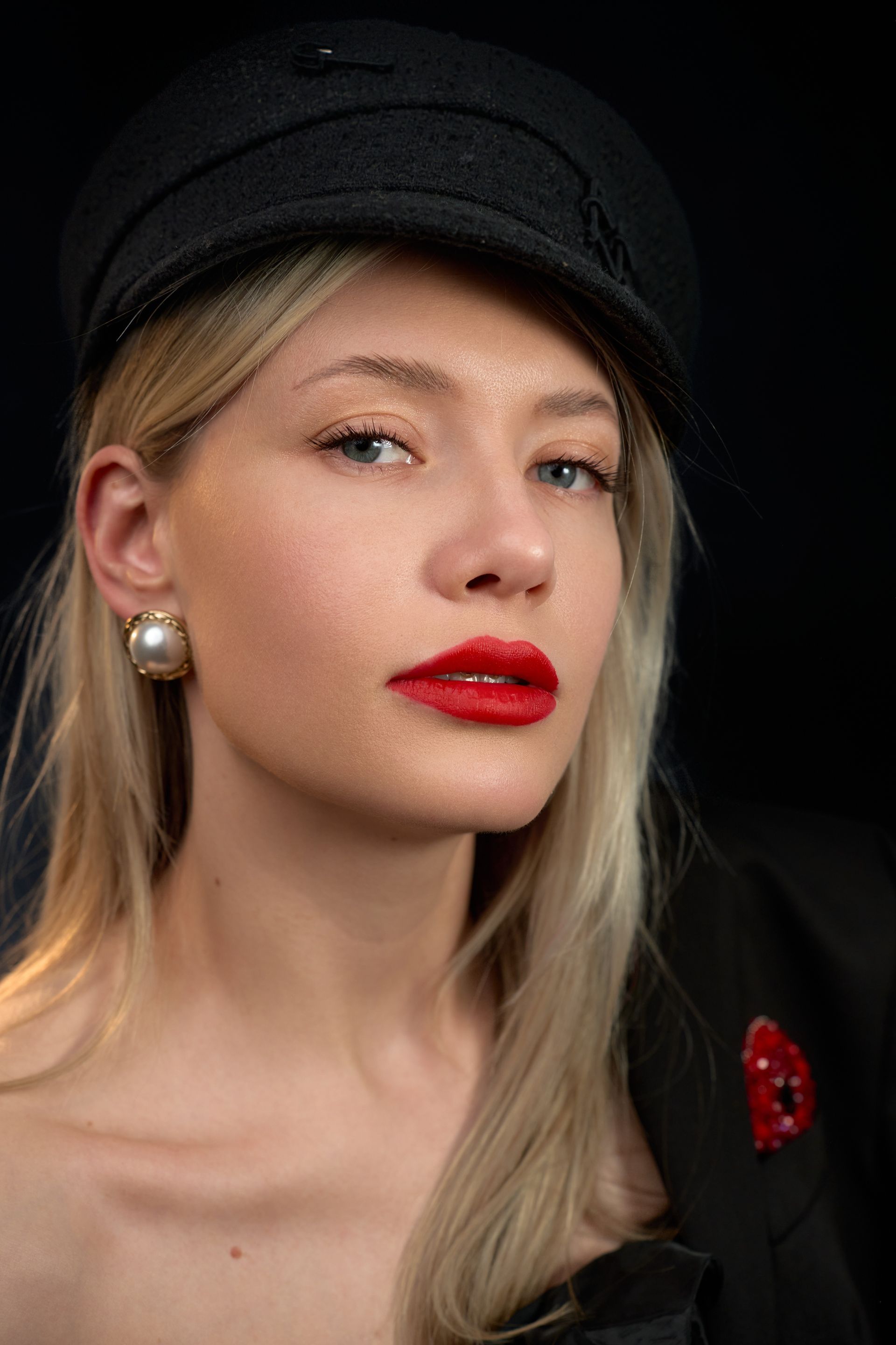 A woman wearing a black hat and red lipstick is looking at the camera.
