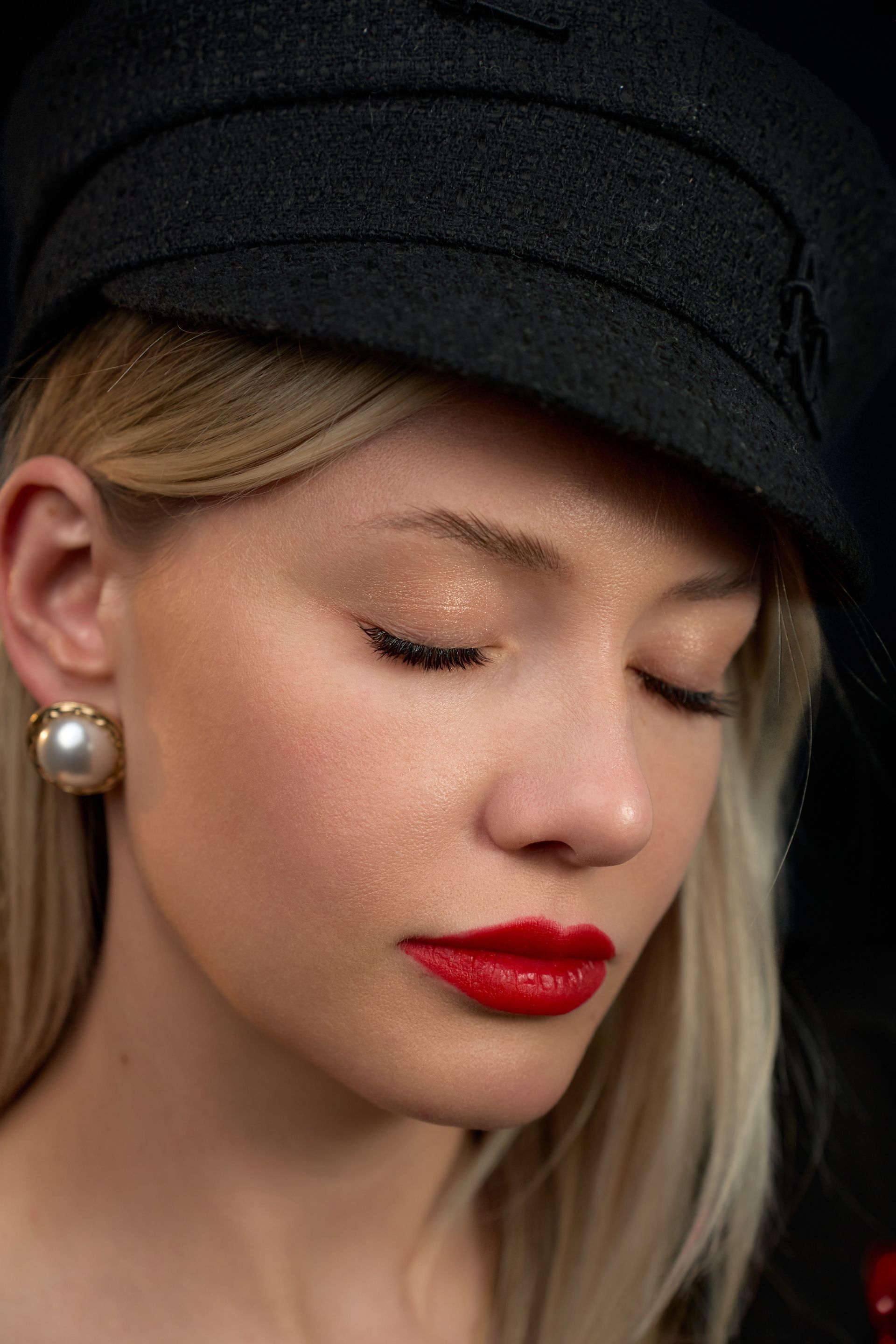 A close up of a woman wearing a hat and red lipstick.