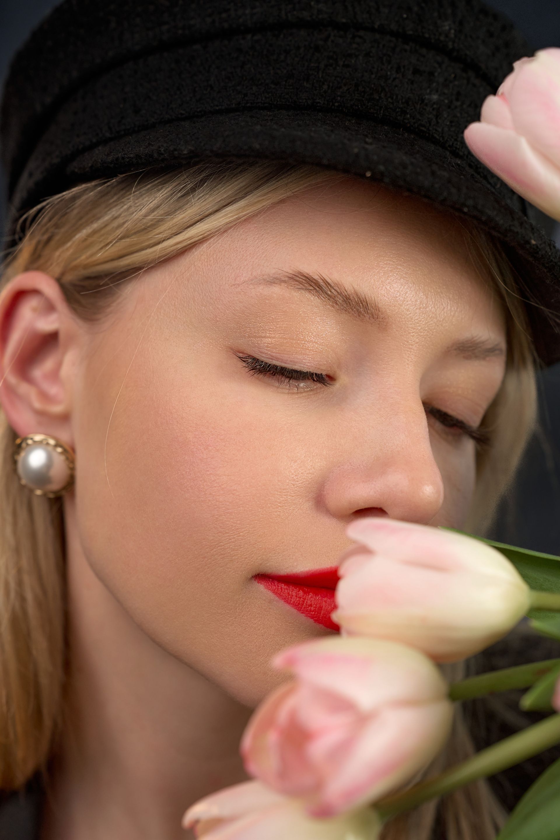 A woman wearing a black hat is smelling a pink flower.