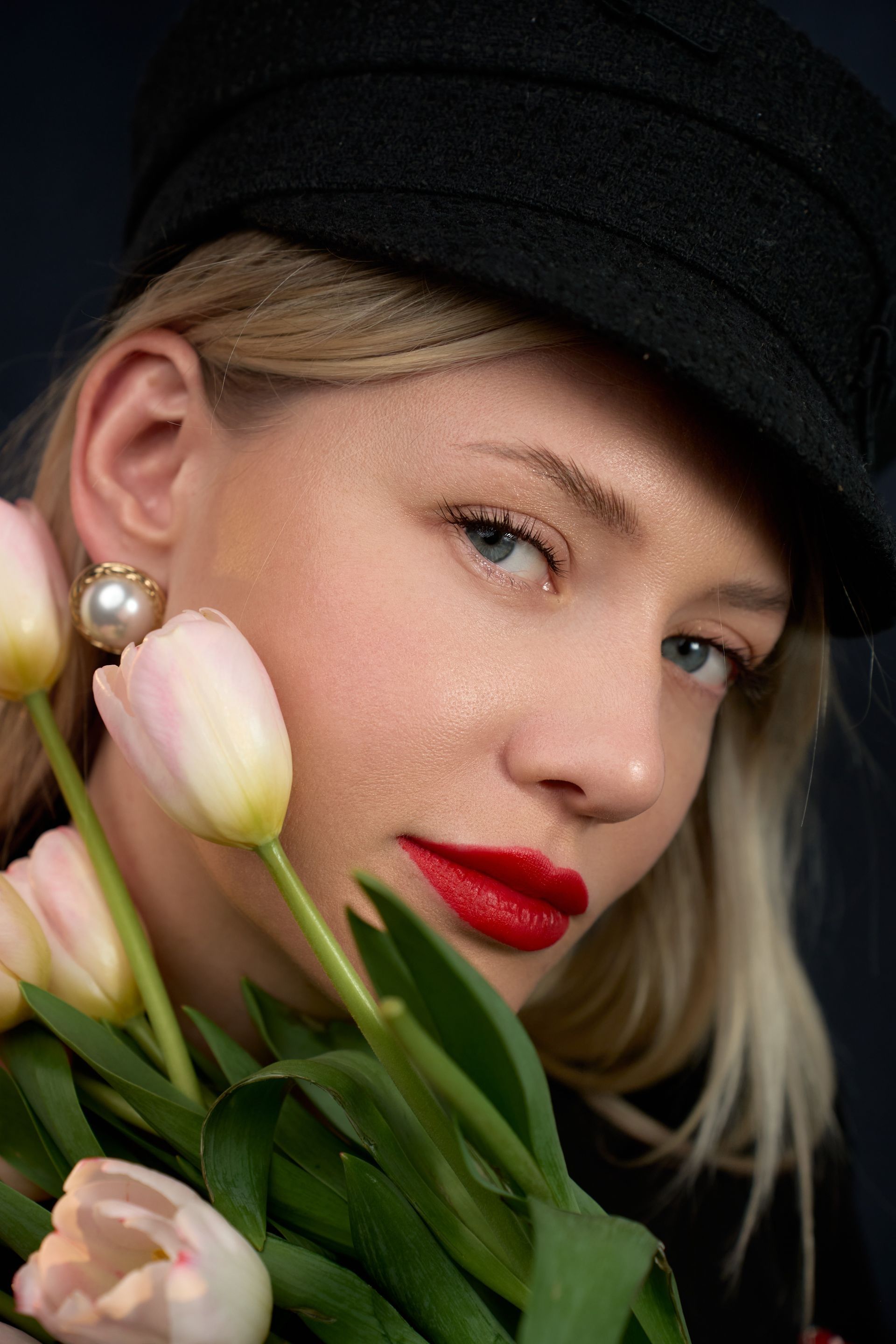 A woman wearing a black hat and red lipstick is holding a bouquet of flowers.