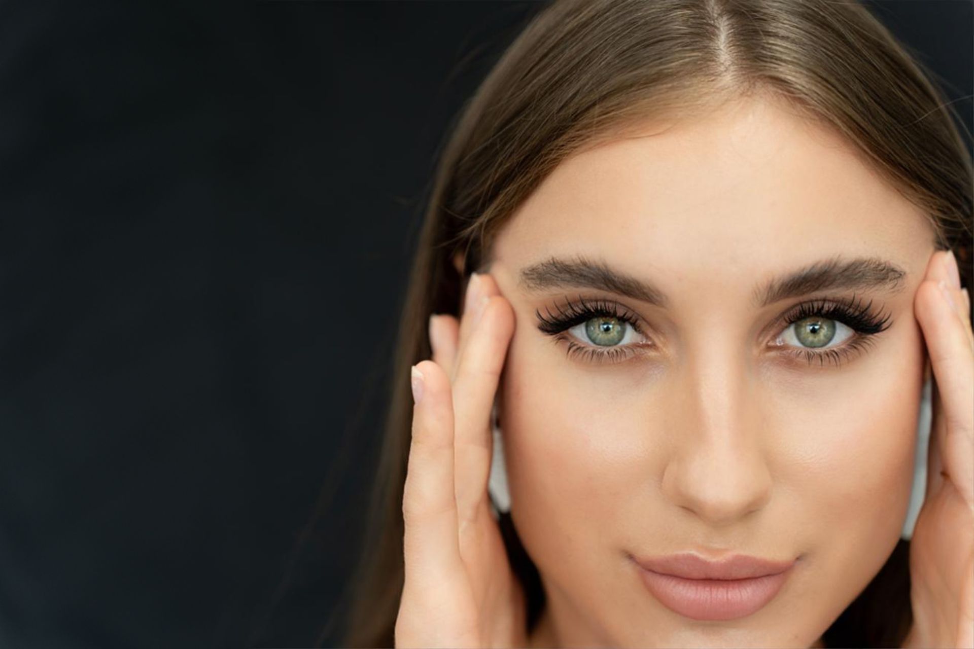 A close up of a woman 's face with her hands on her forehead.