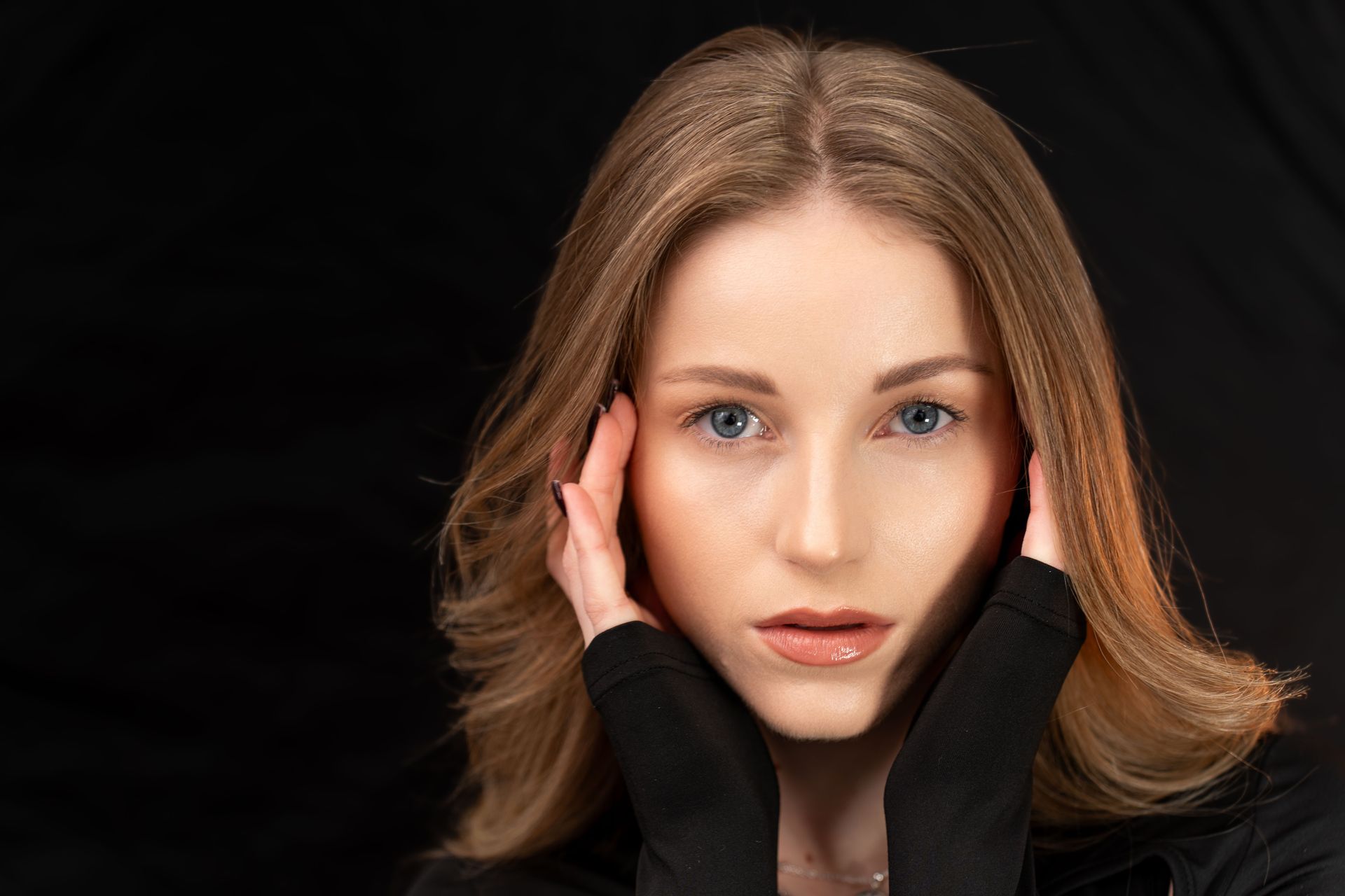 A woman is covering her ears with her hands and looking at the camera.