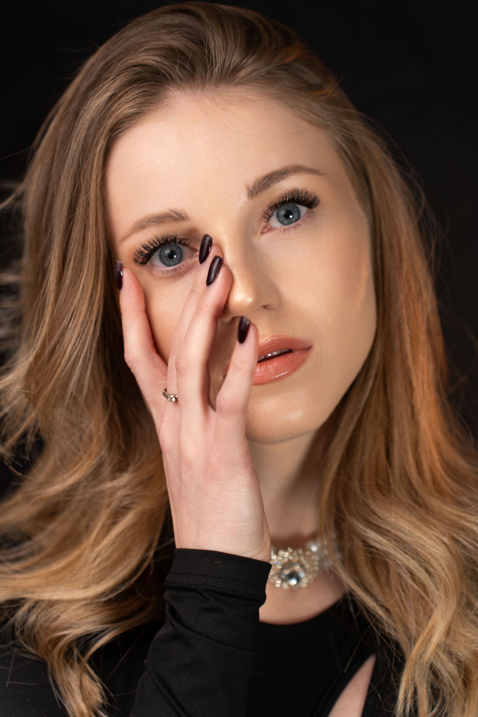 A woman with long blonde hair is covering her face with her hand.