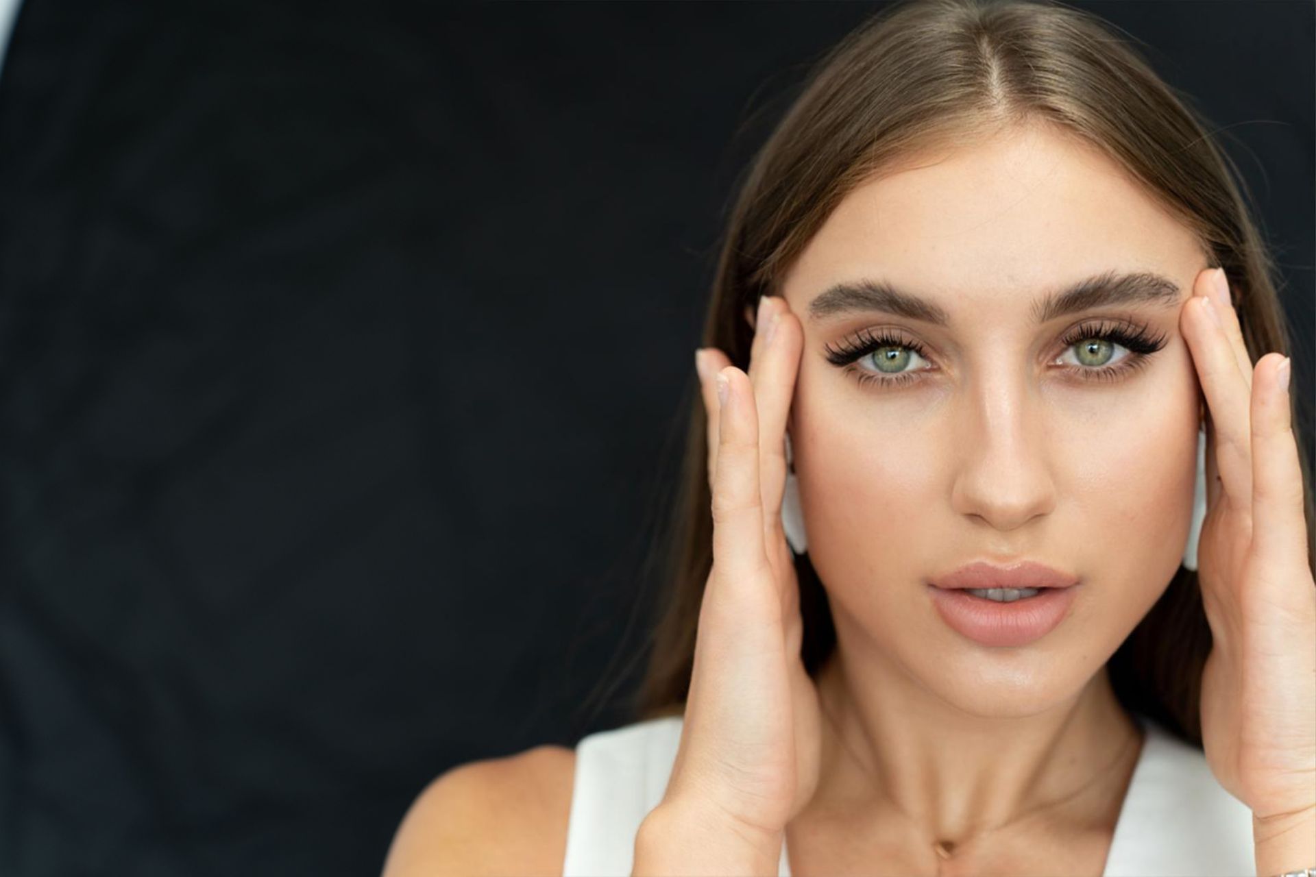 A woman is holding her head with her hands and looking at the camera.
