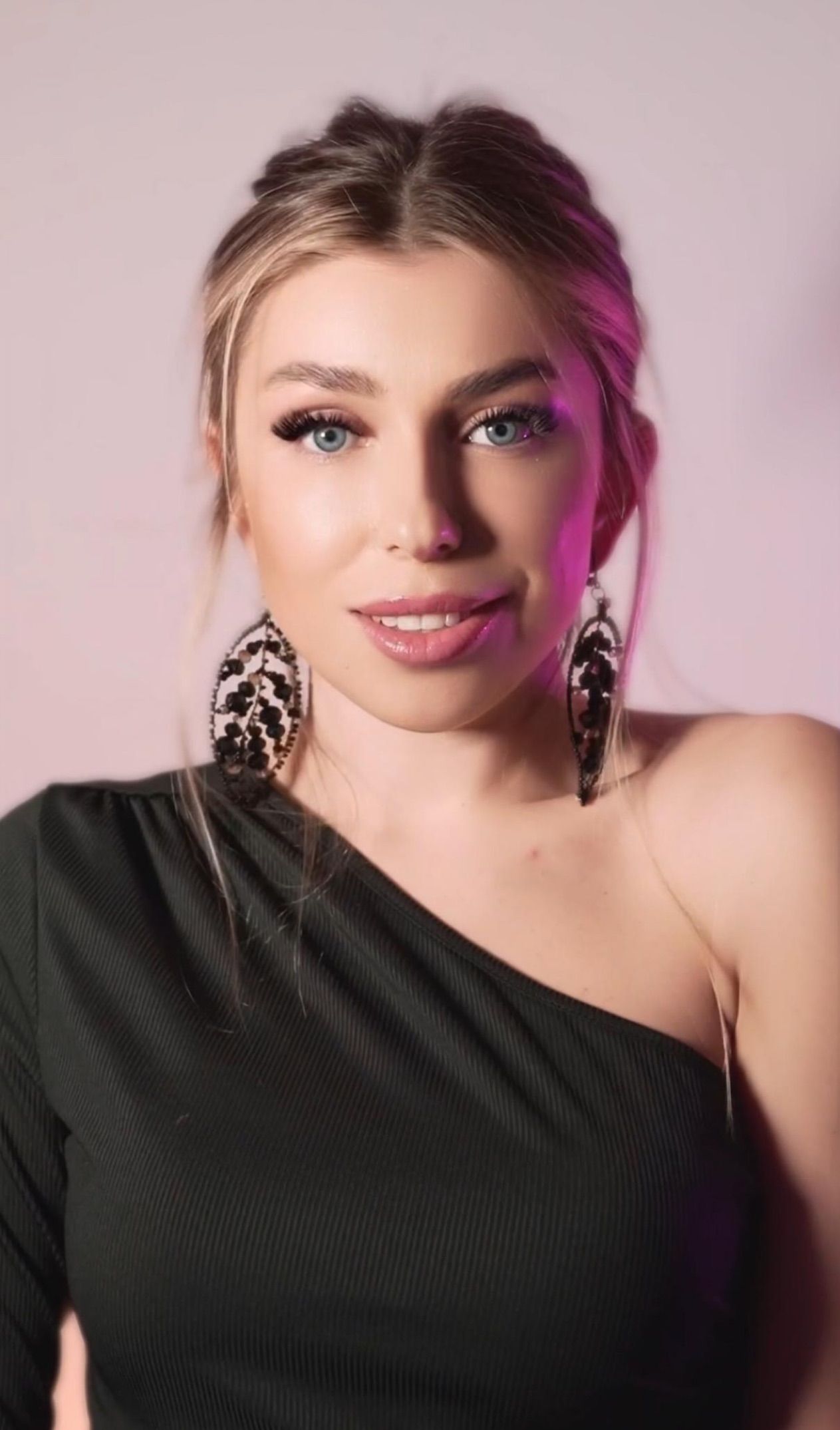 A woman wearing a black one shoulder top and feather earrings