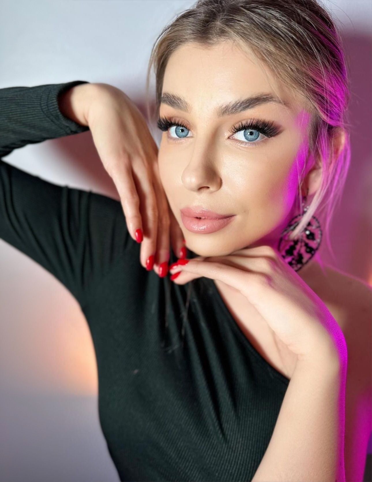 A woman with blue eyes and red nails is wearing a black dress and earrings.