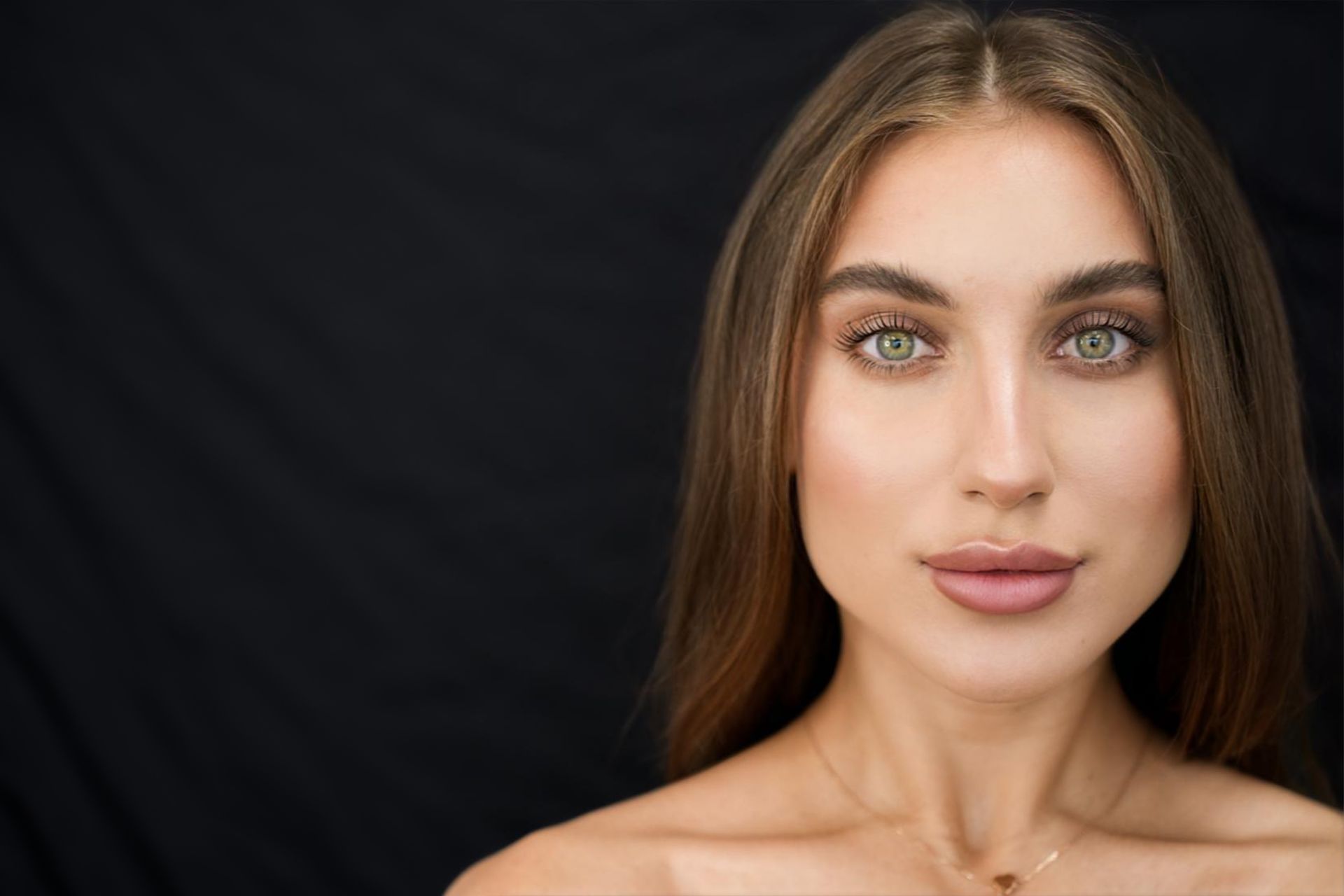 Woman with green eyes and brown hair, looking at the camera against a black backdrop.