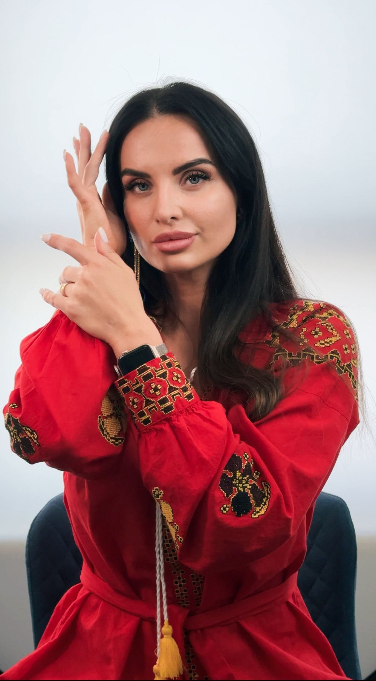 A woman in a red dress is sitting in a chair with her hands on her face.