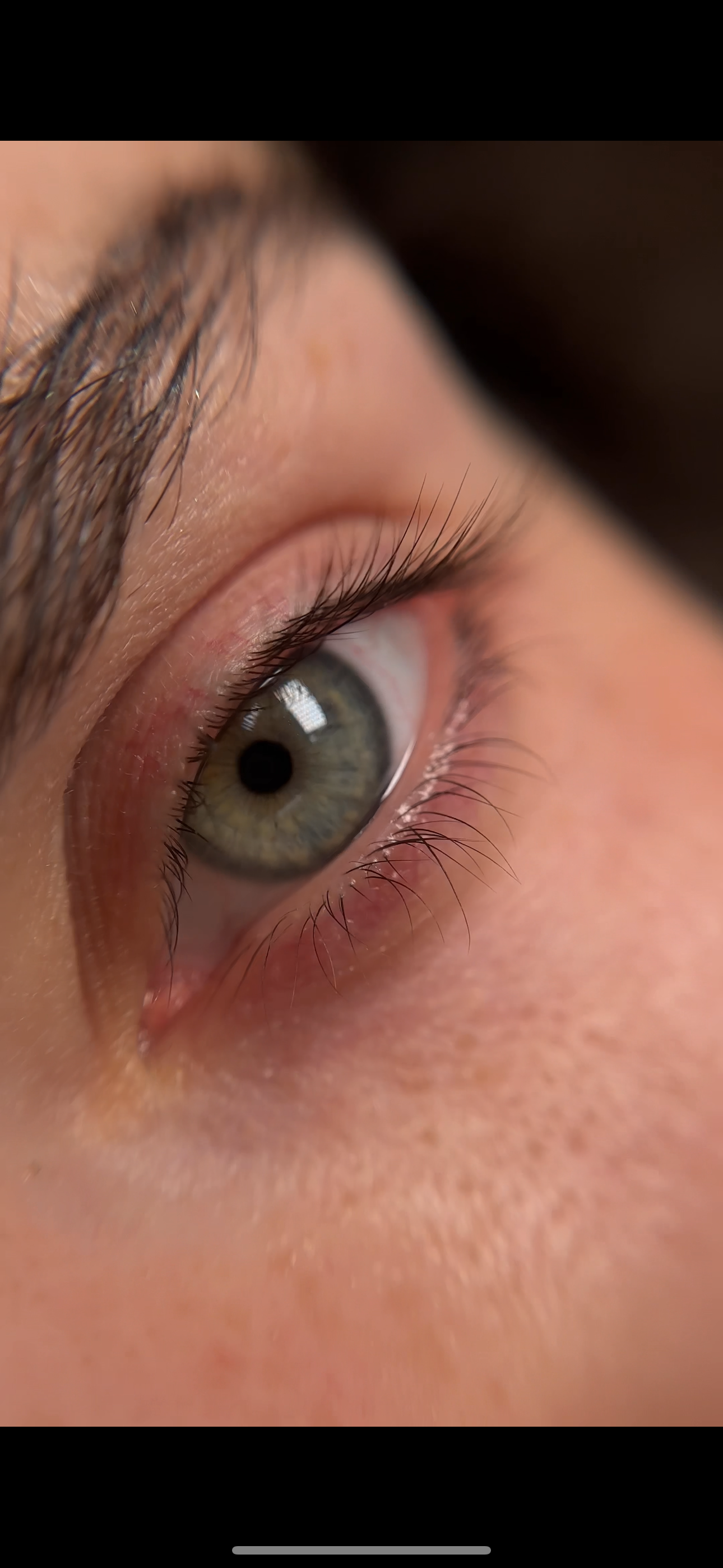 A close up of a person 's green eye with long eyelashes.