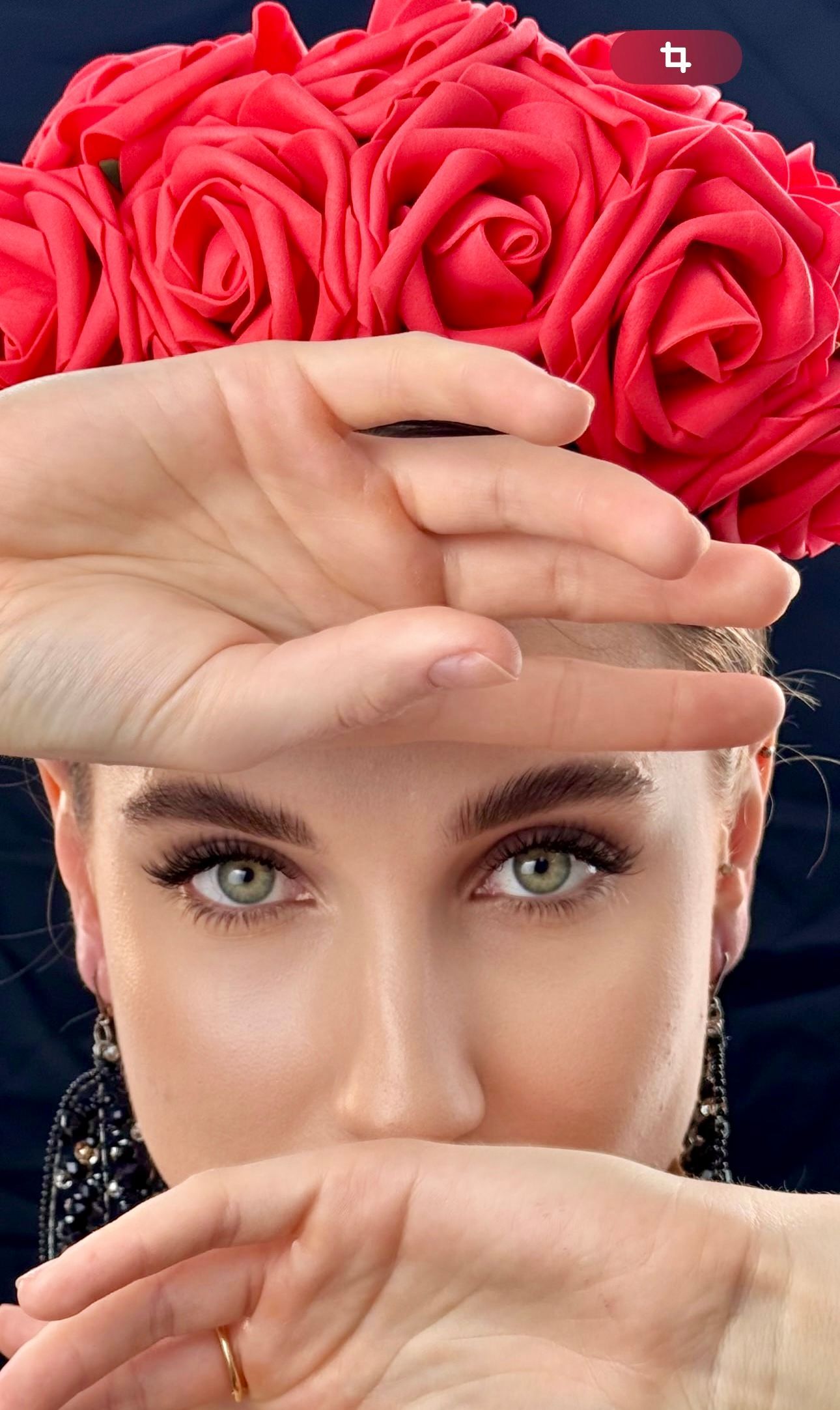 A woman covering her face with her hands with a bouquet of red roses in the background.