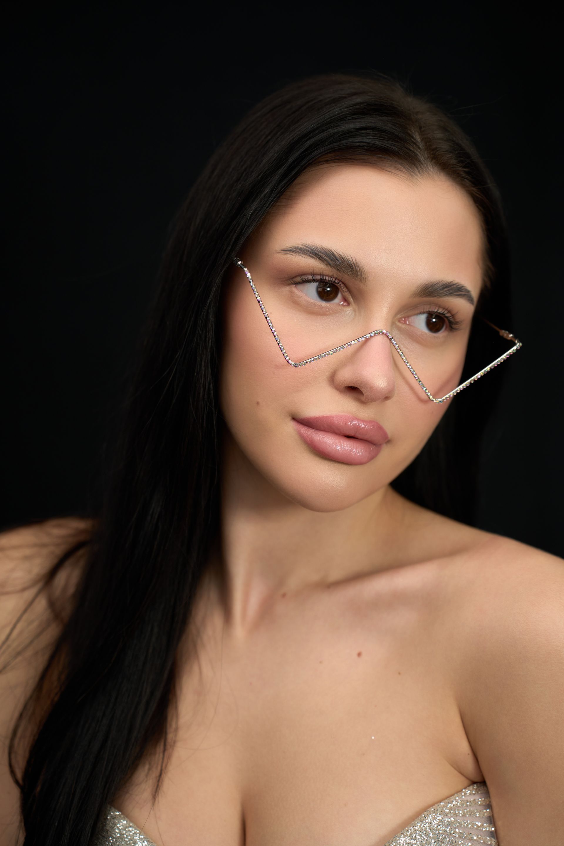 A woman wearing glasses and a nose chain on a black background.