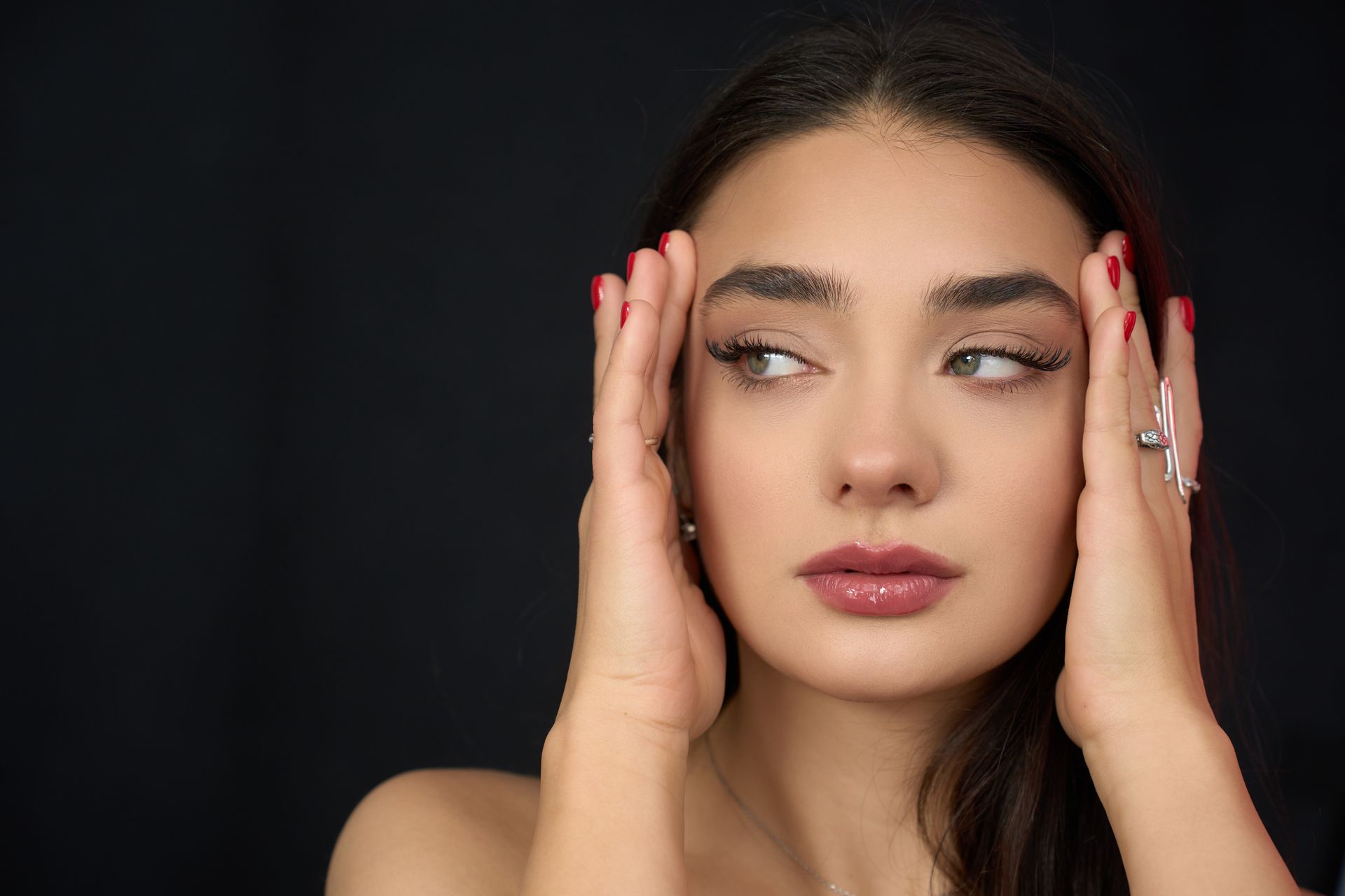 A close up of a woman 's face with her hands on her forehead.
