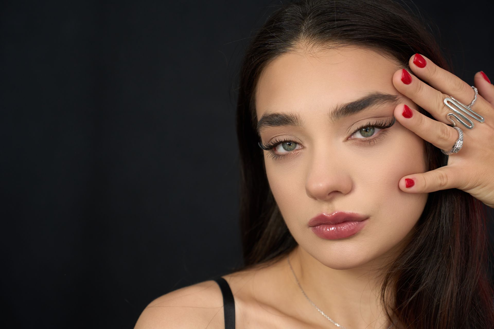 A woman with red nails and a ring on her finger is touching her face.