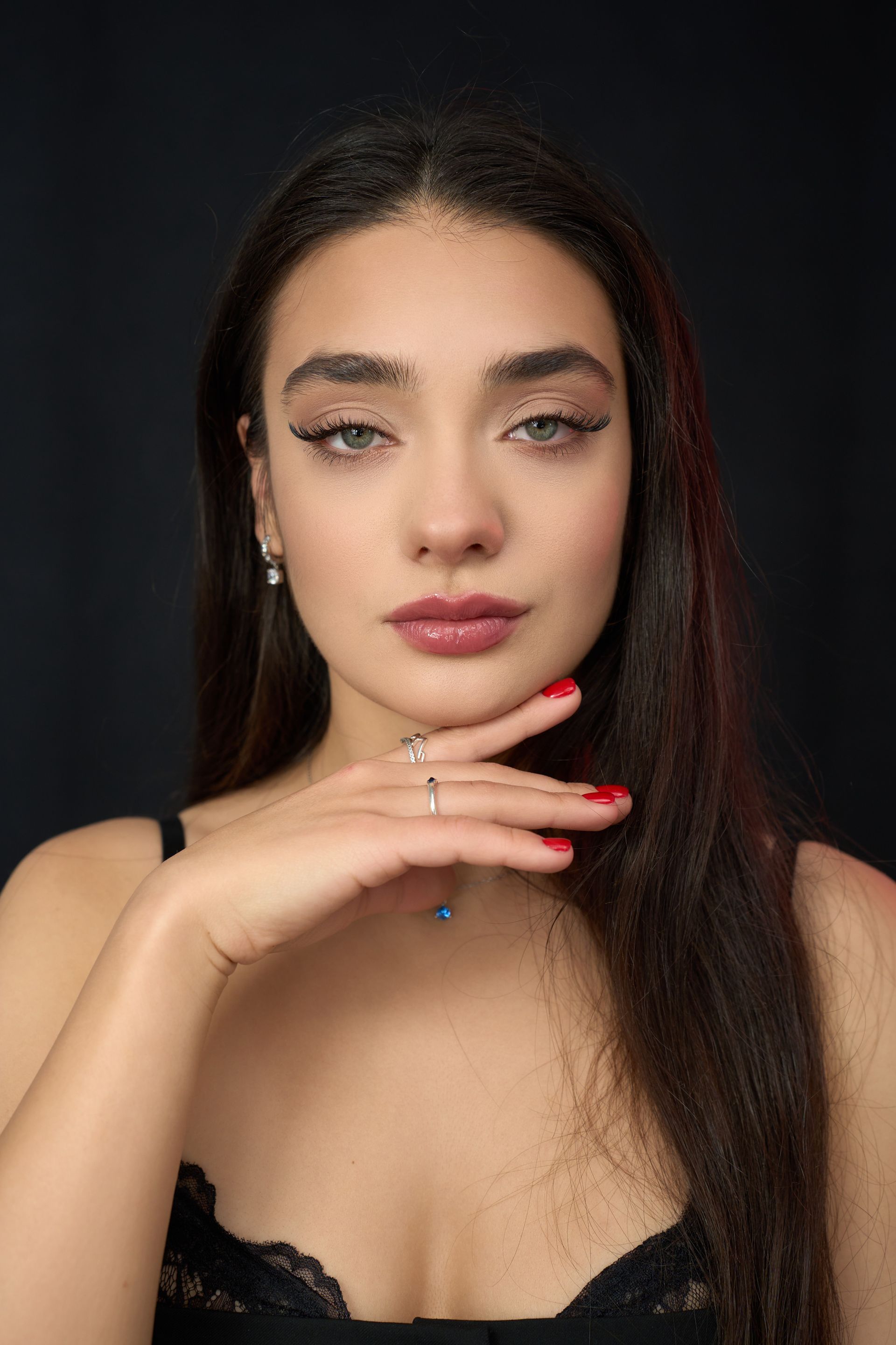 A woman with long hair and red nails is holding her hand to her face.