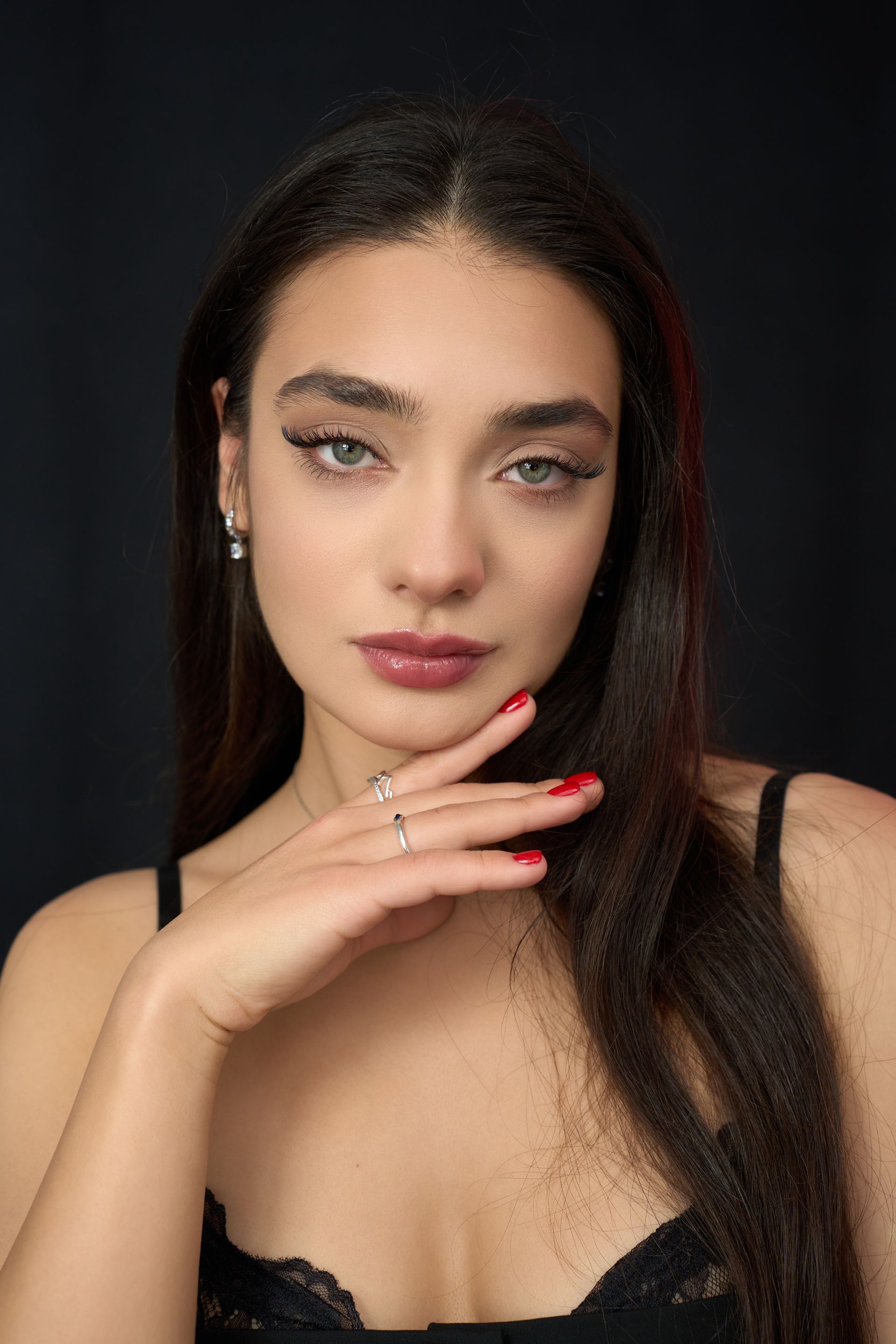 A woman with long hair and red nails is holding her hand to her face.
