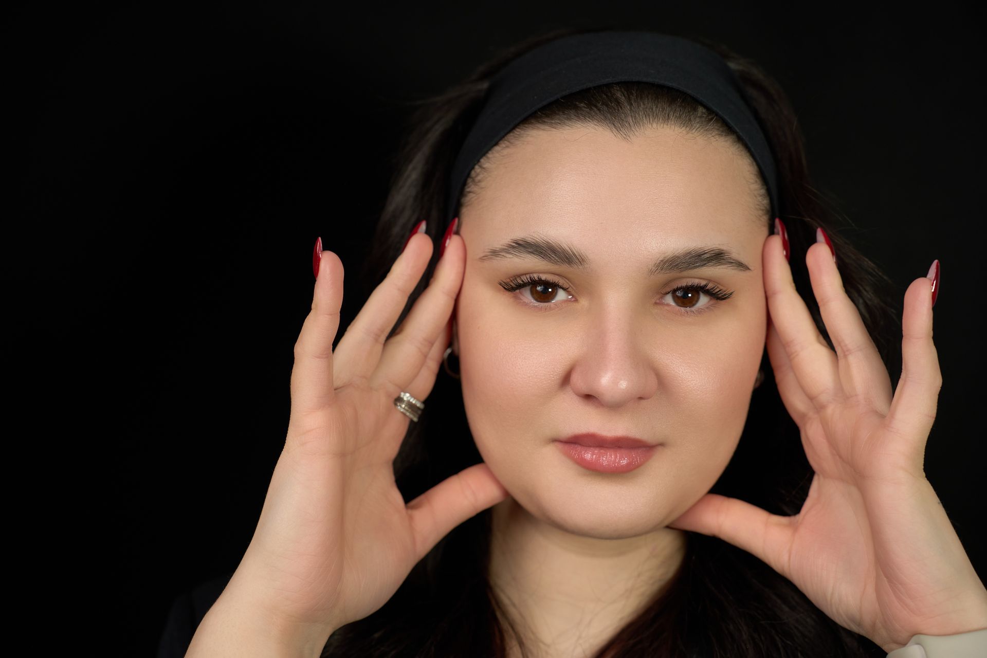 A woman is holding her head with her hands while wearing a headband.