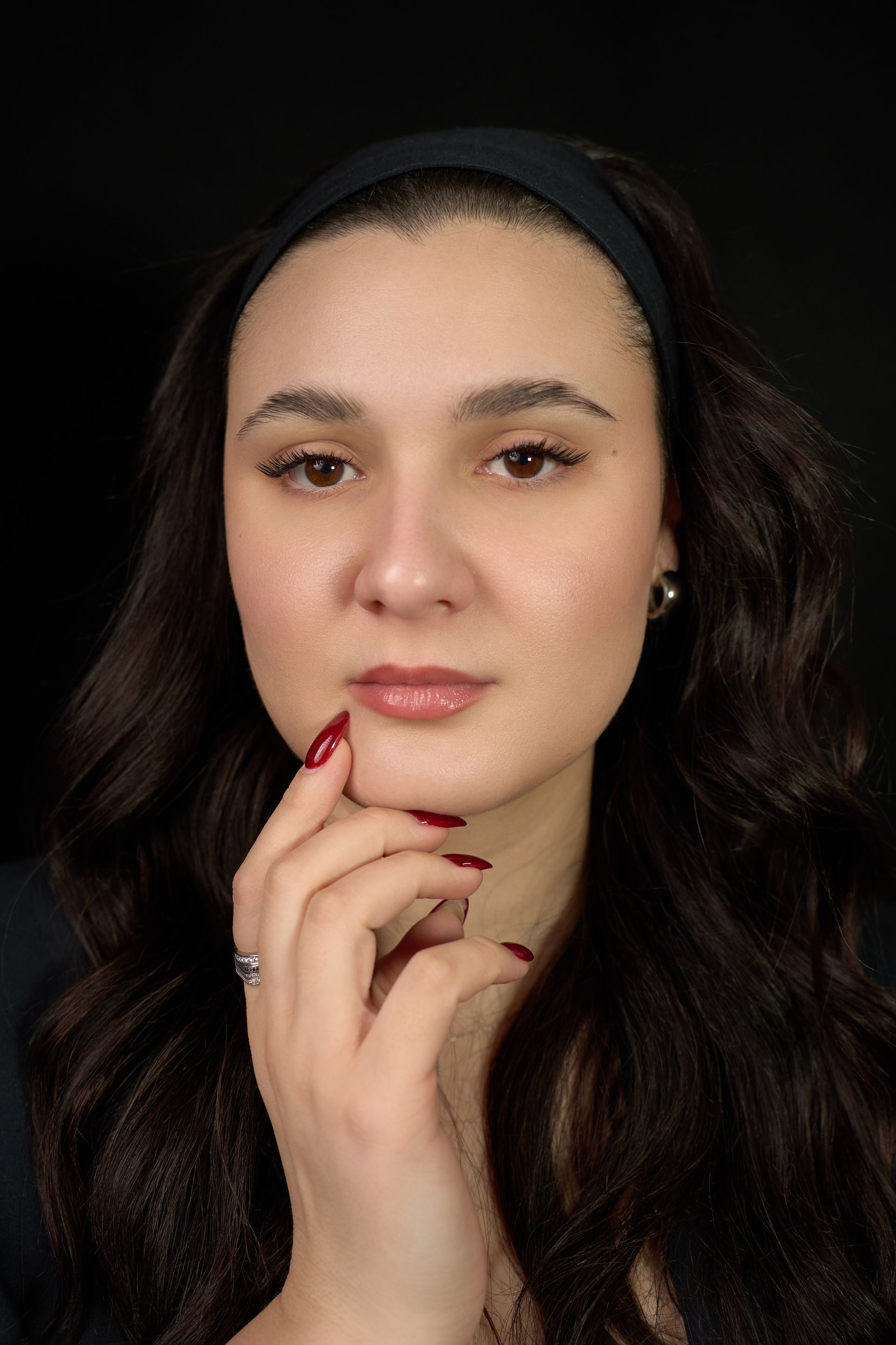 A woman with red nails is holding her hand to her face.