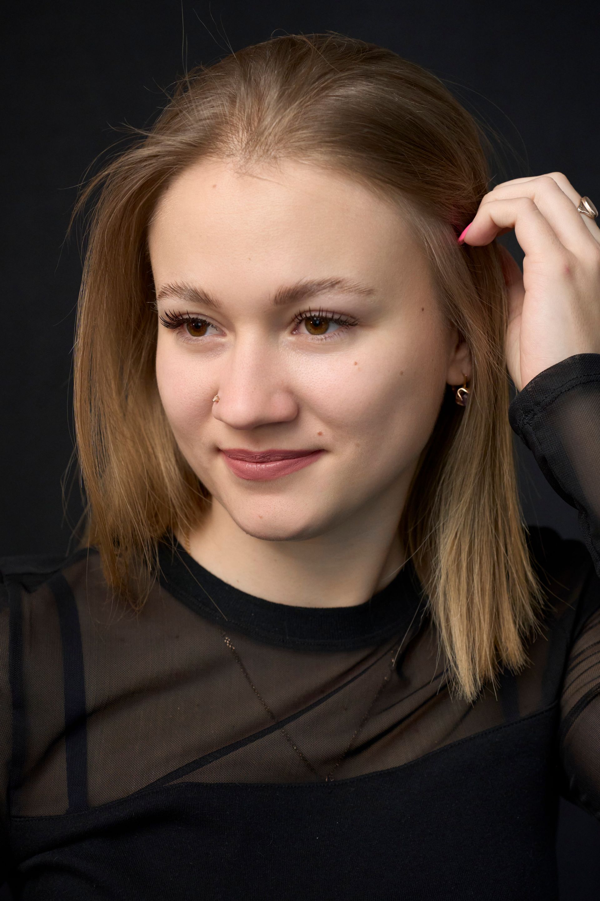 A woman in a black shirt is touching her hair.