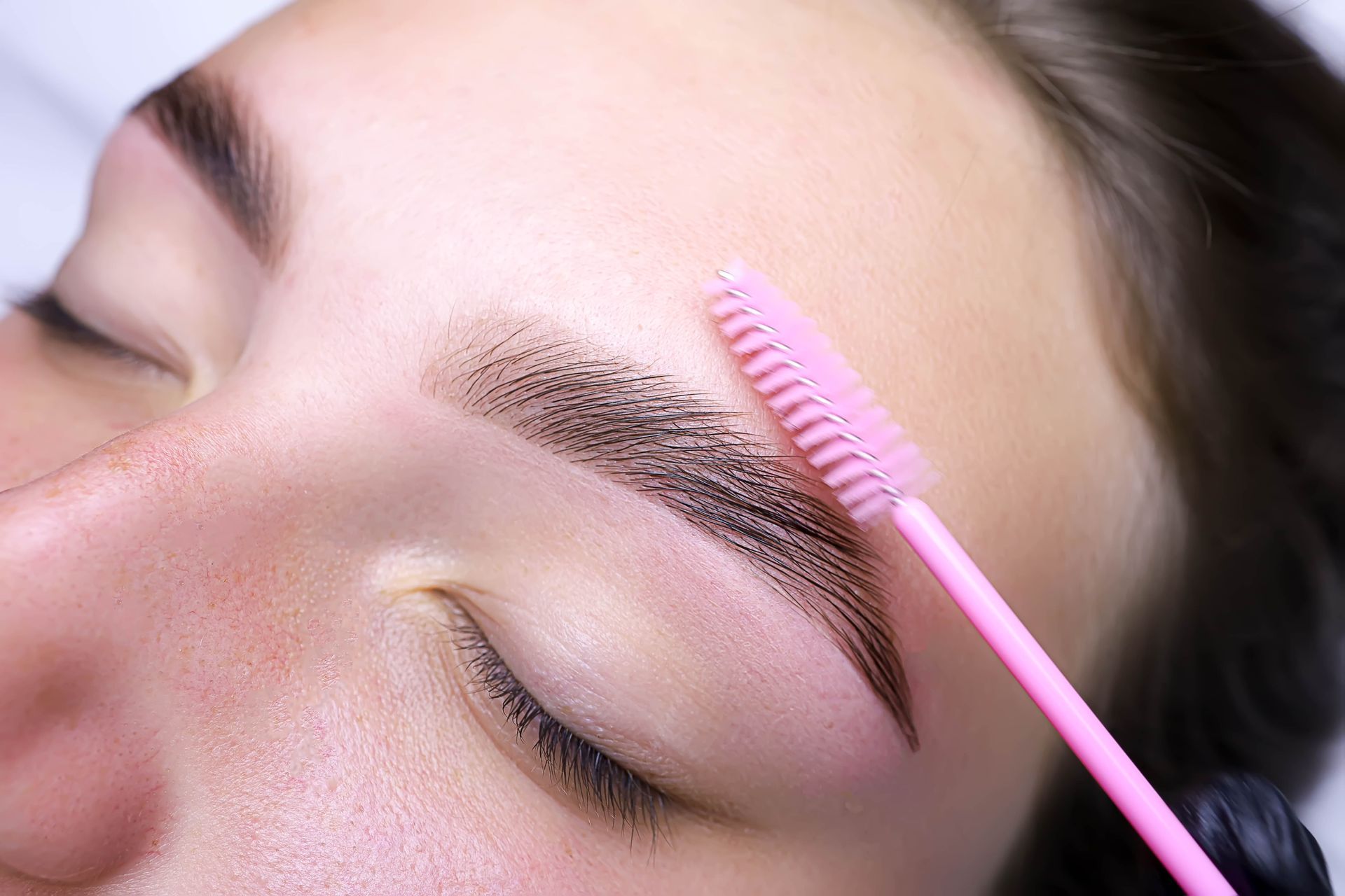 A woman is getting her eyebrows done with a pink brush.