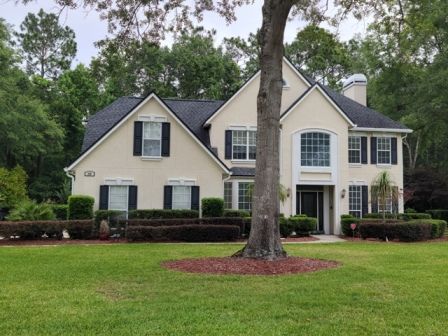 A large white house with black shutters and a tree in front of it
