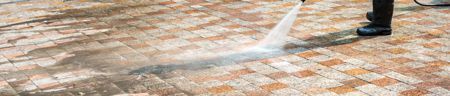 A person is using a high pressure washer to clean a brick floor.