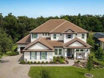 An aerial view of a large white house with a brown roof surrounded by trees.