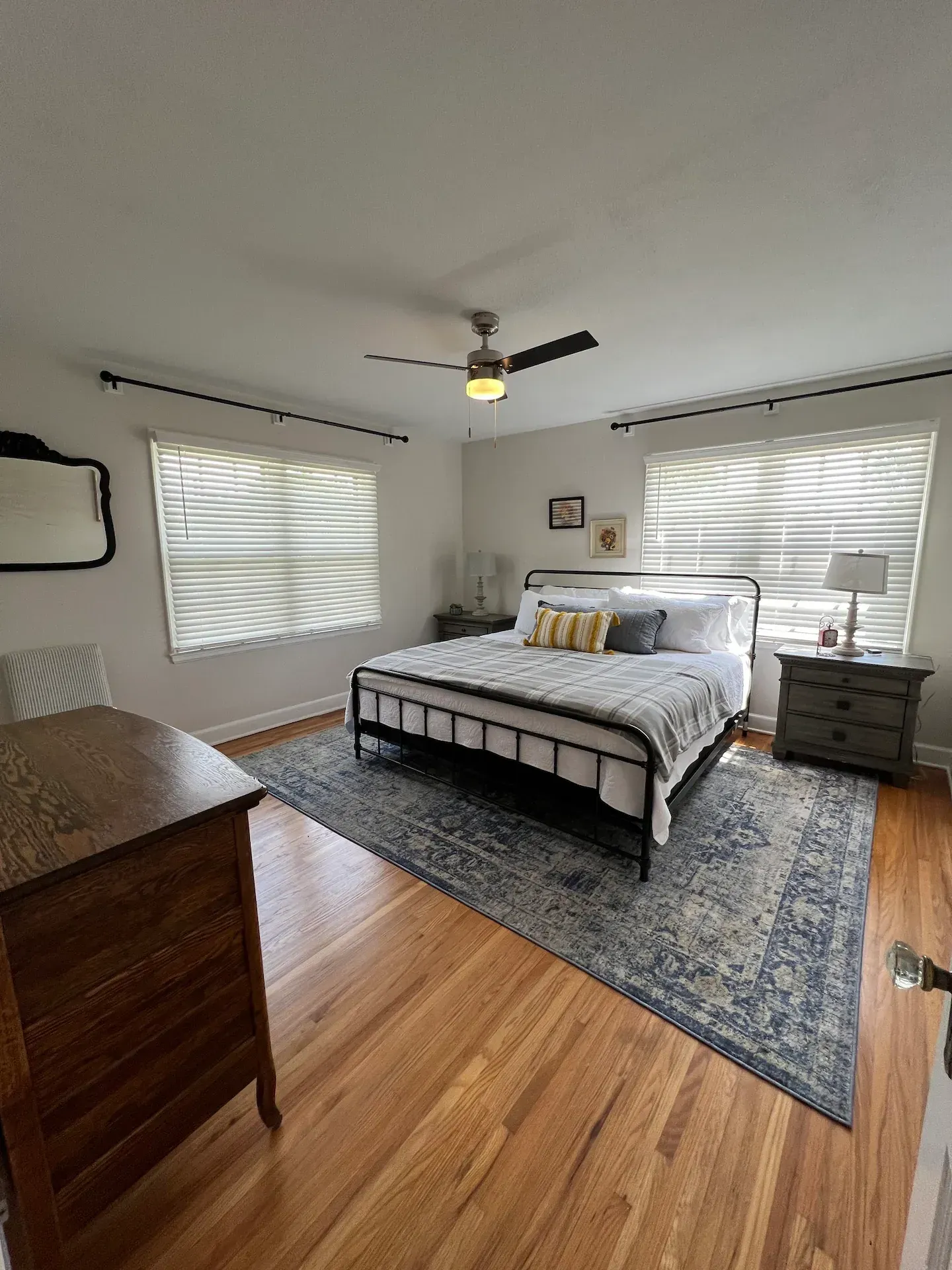 A bedroom with a bed , dresser , nightstand , mirror and ceiling fan.