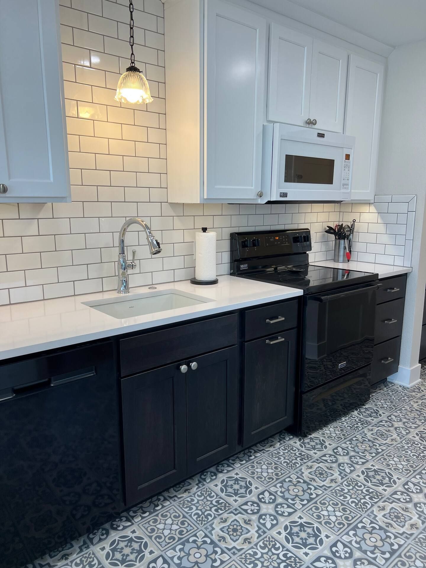 A kitchen with black cabinets , white counter tops , a stove , and sink.