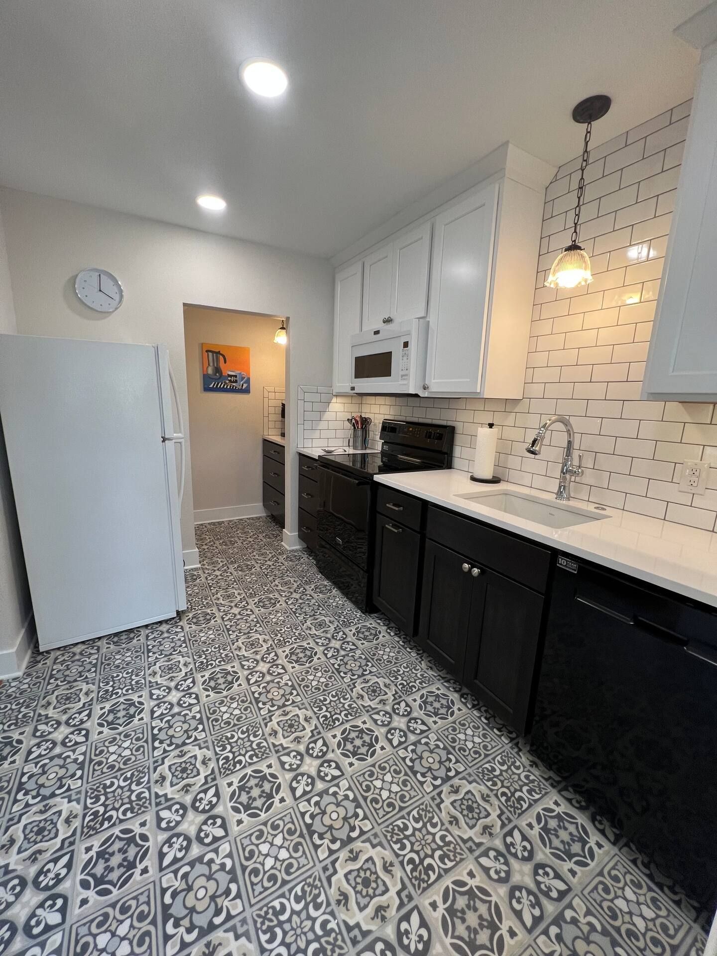 A kitchen with black cabinets , a white refrigerator , a sink , and a clock on the wall.