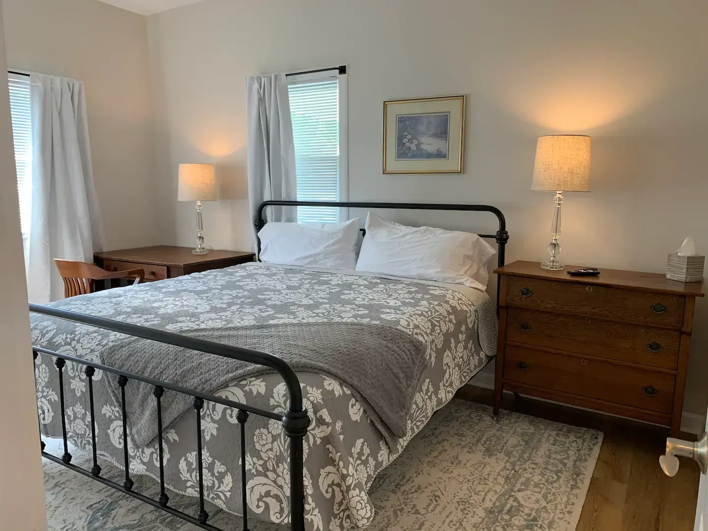 A bedroom with a bed , dresser , desk and two lamps.