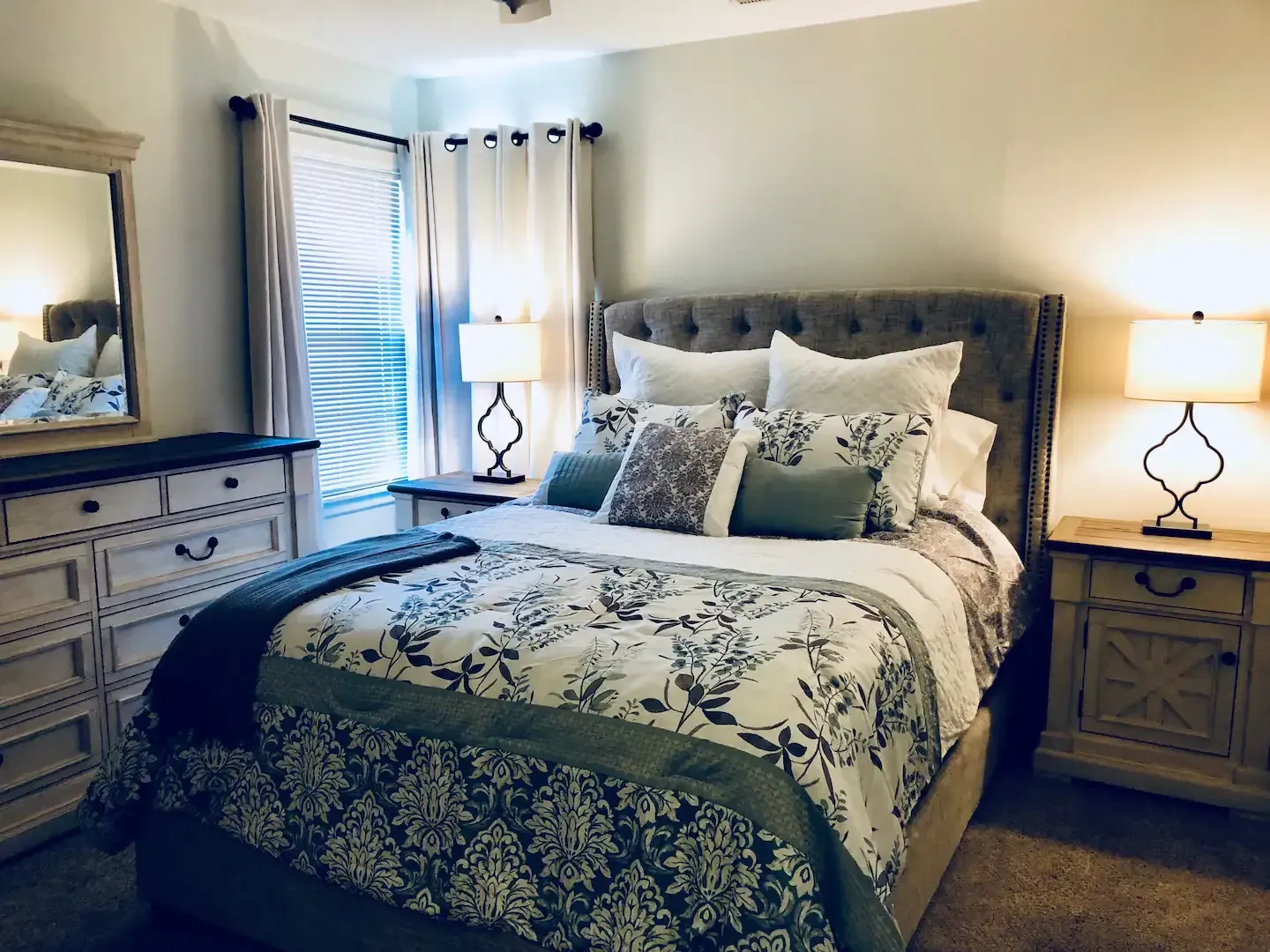A bedroom with a bed , dresser , nightstand and mirror.