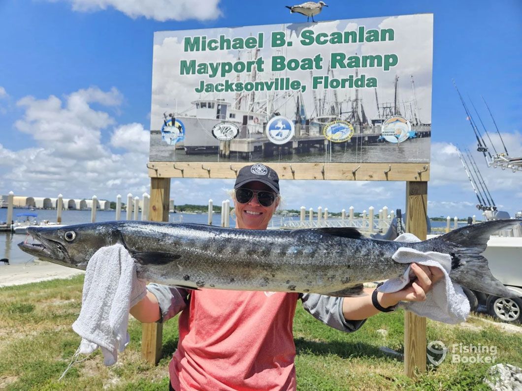 A man is holding a large fish in front of a sign.