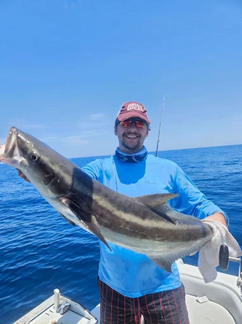A man is holding a large fish on a boat in the ocean.