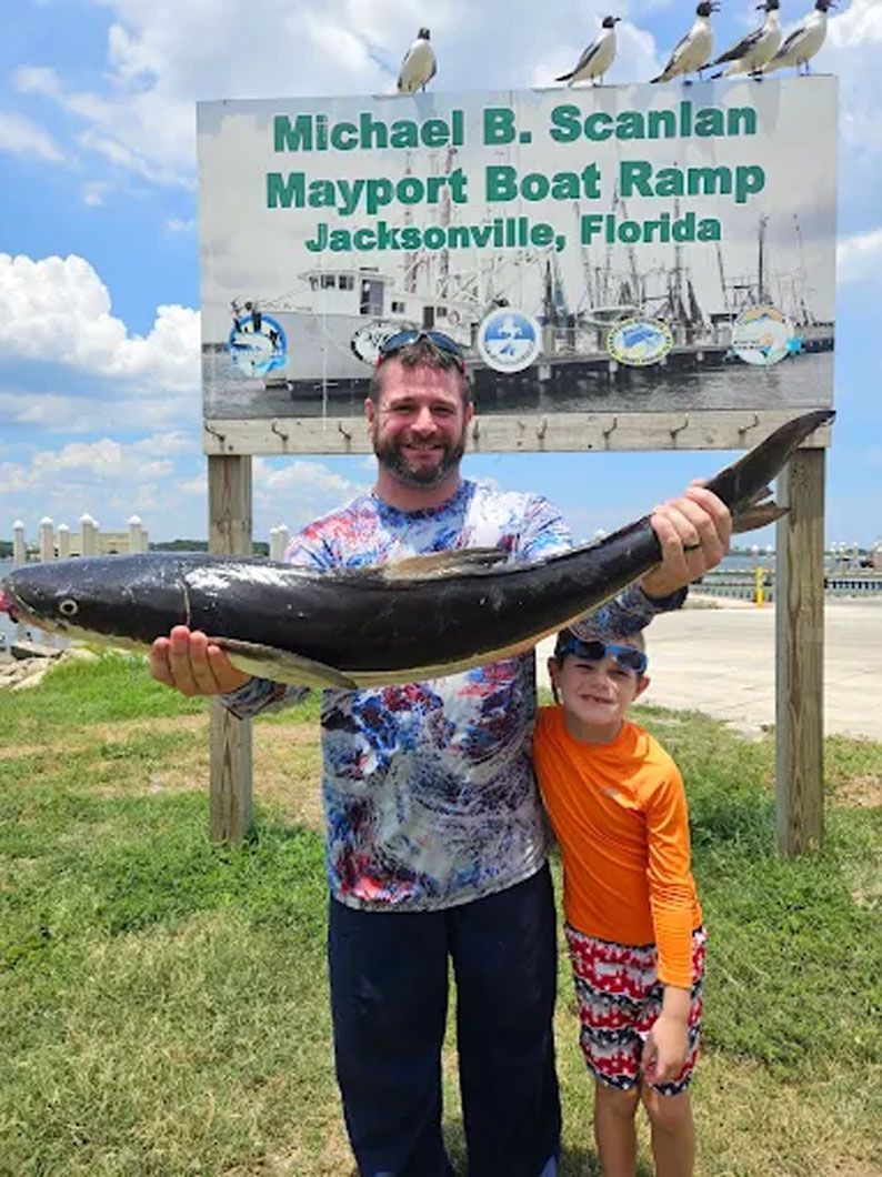 A man and a boy are holding a large fish in front of a sign.