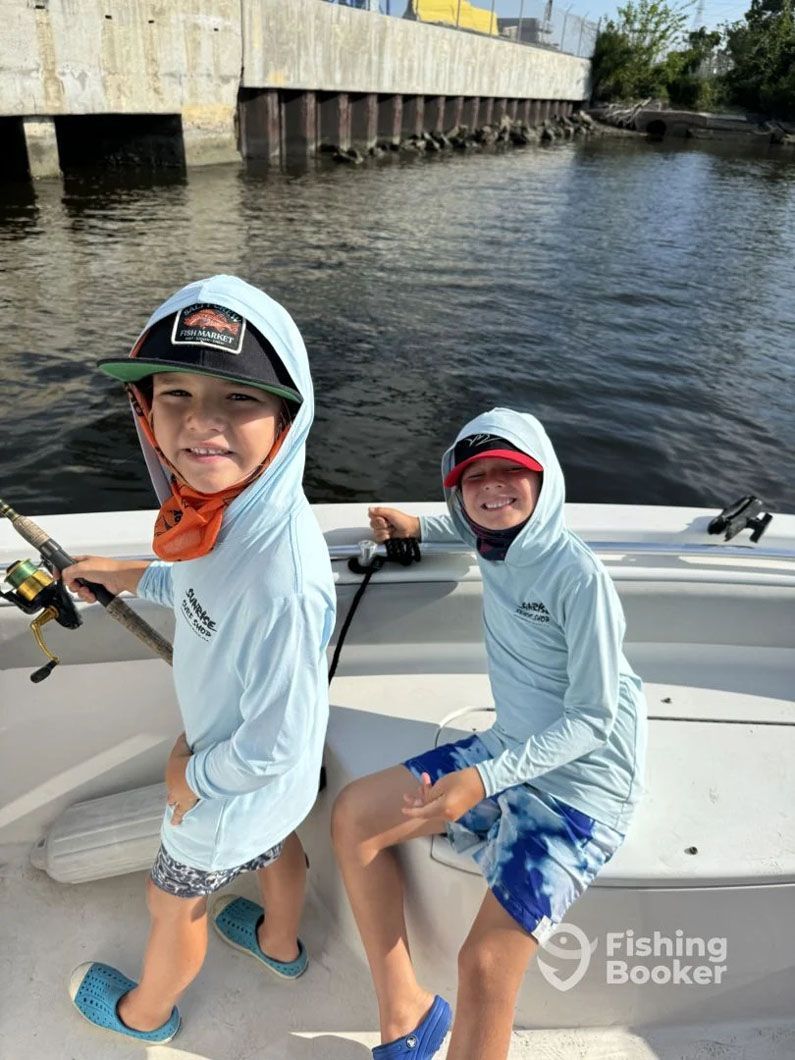Two young boys are sitting on a boat holding fishing rods.