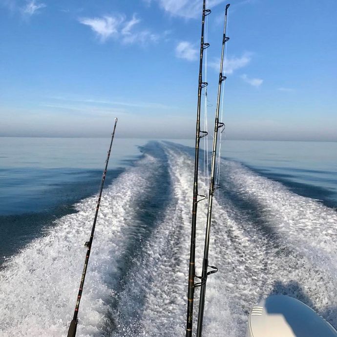 A boat is going through the ocean with fishing rods on the back of it.