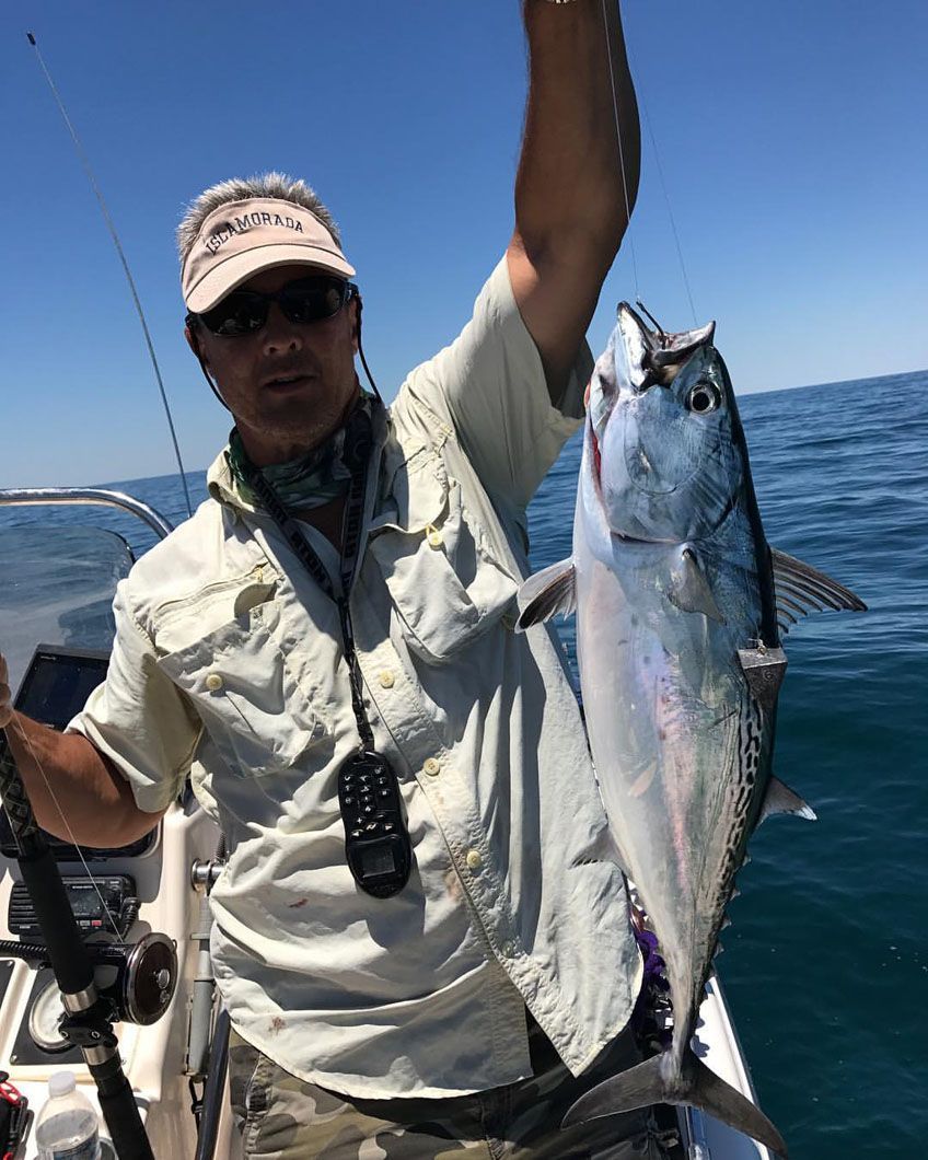 A man is holding a fish in his hand on a boat in the ocean.