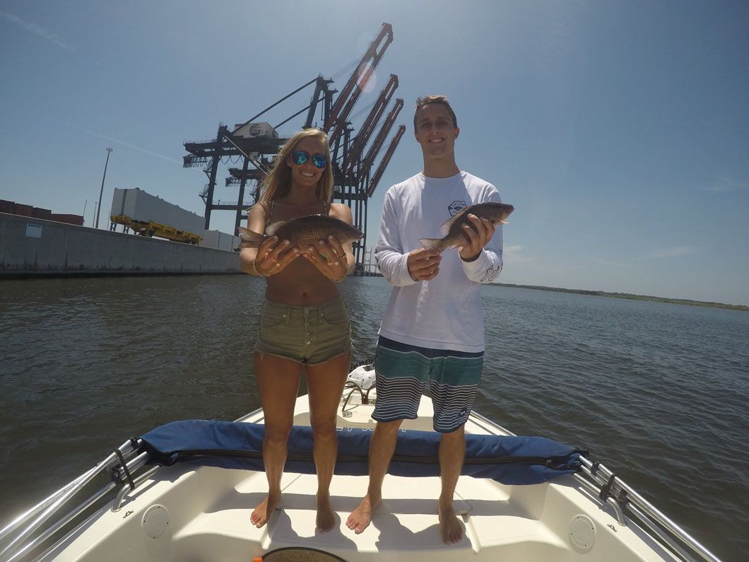 A man and a woman are standing on a boat holding fish.