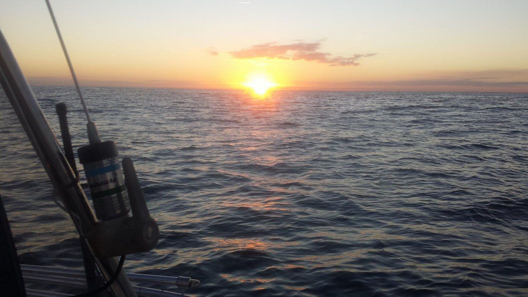 The sun is setting over the ocean from a boat.