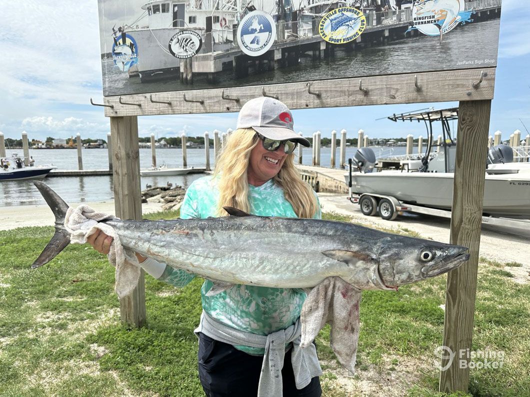 A woman is holding a large fish in front of a sign.