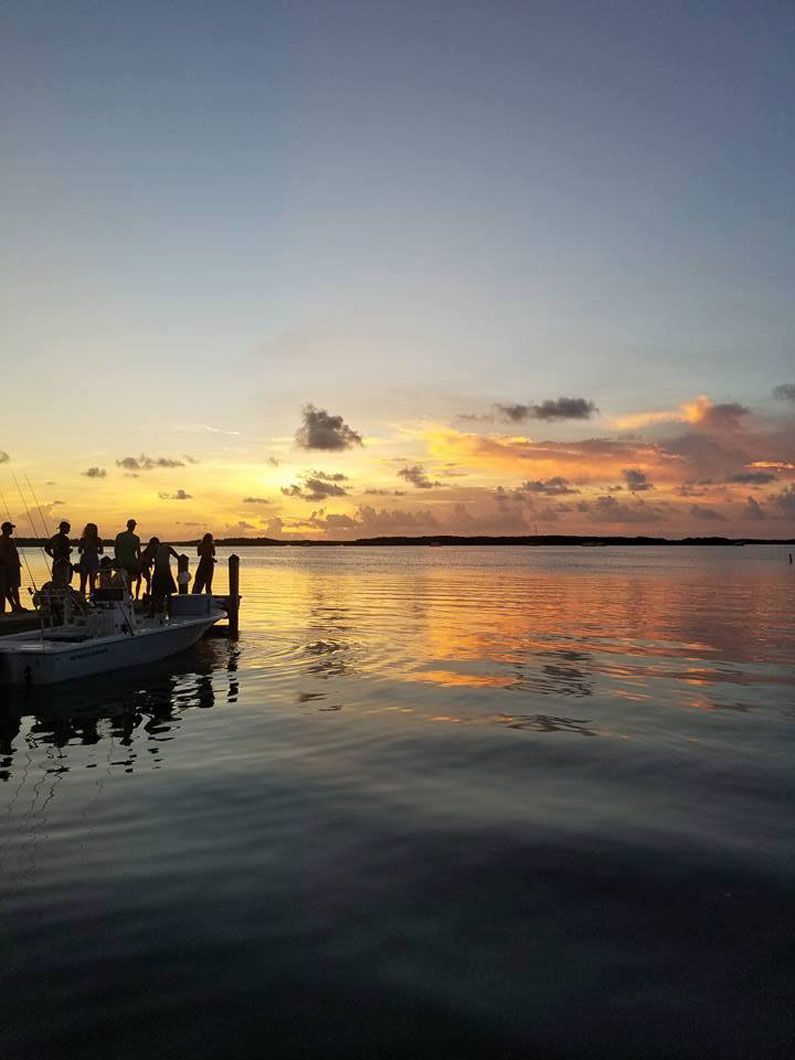 A group of people are standing on a dock overlooking a body of water at sunset.