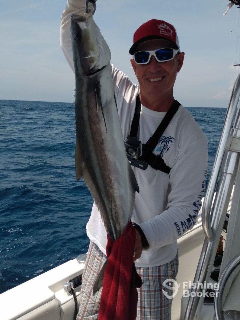A man on a boat holding a fish with fishing booker written on the bottom