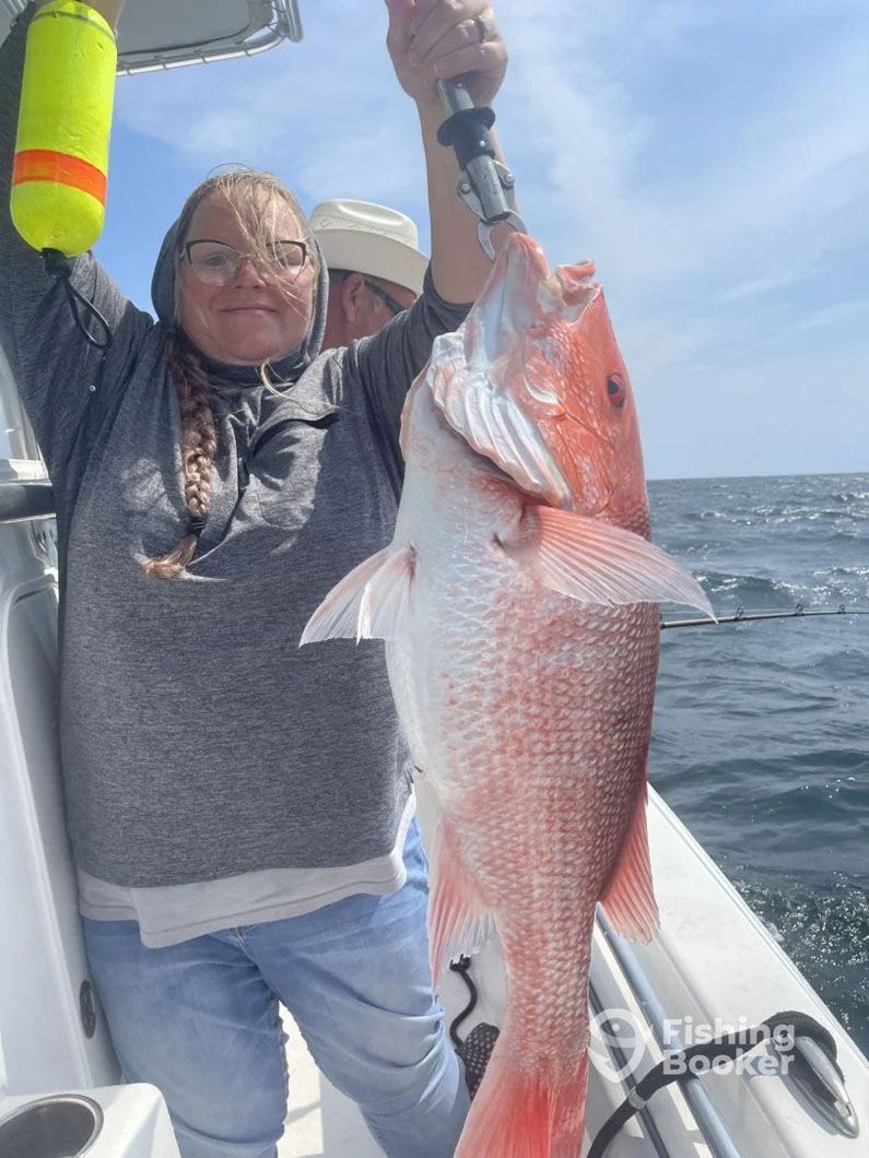A woman is holding a large red fish on a boat.